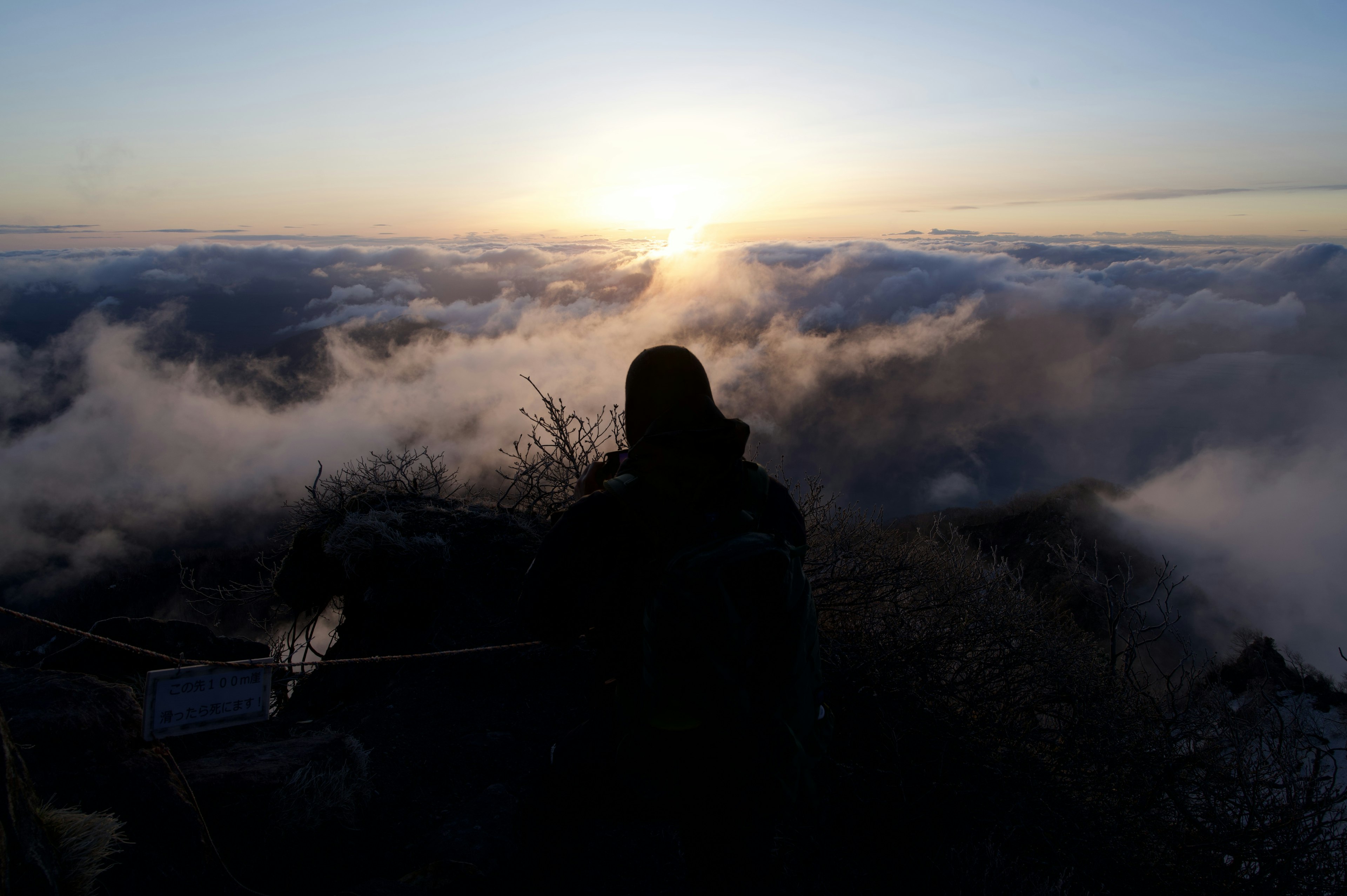 山の頂上から雲海を見下ろす人物のシルエットと朝日