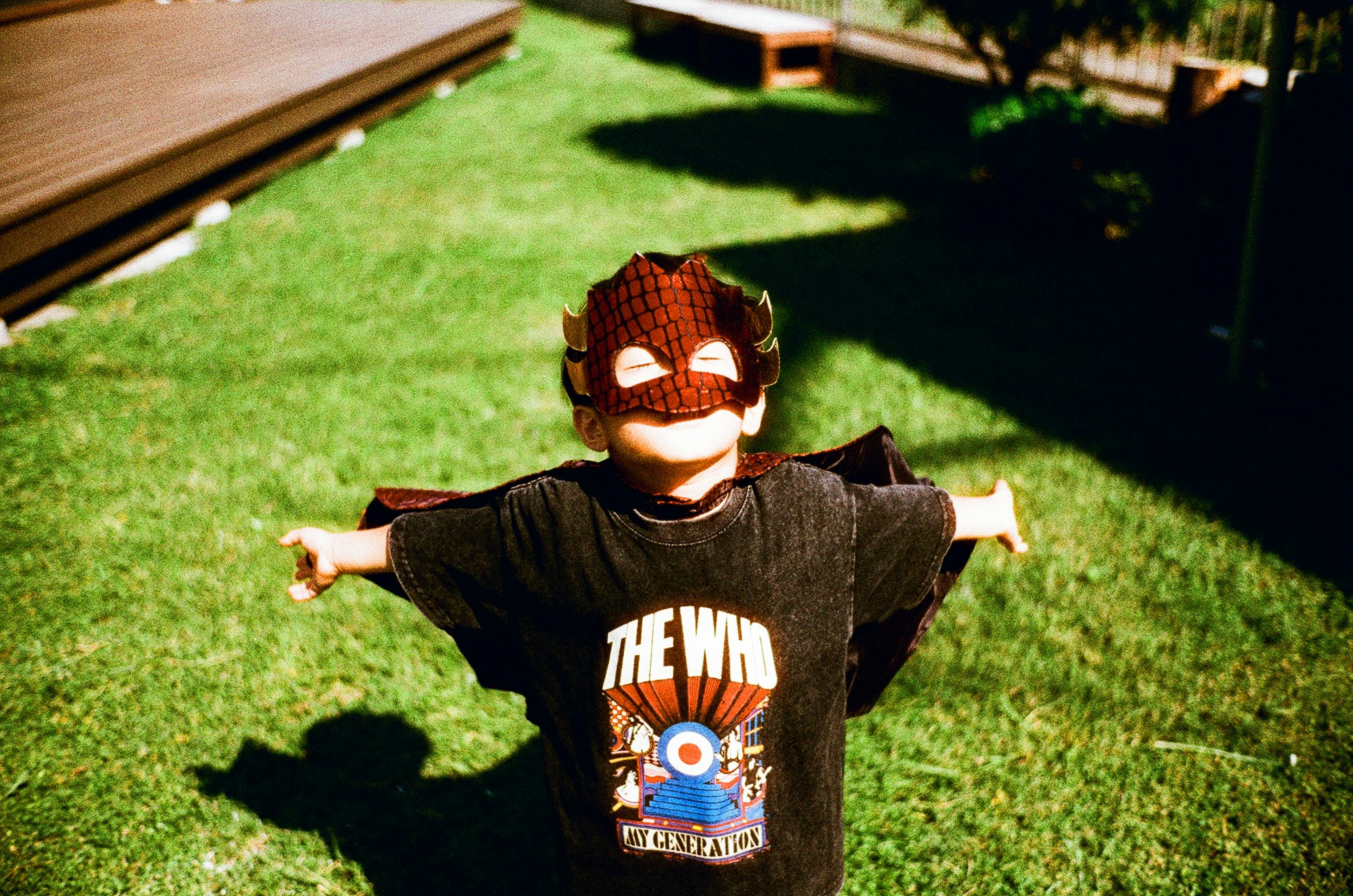 Child dressed as a superhero posing with arms outstretched on green grass