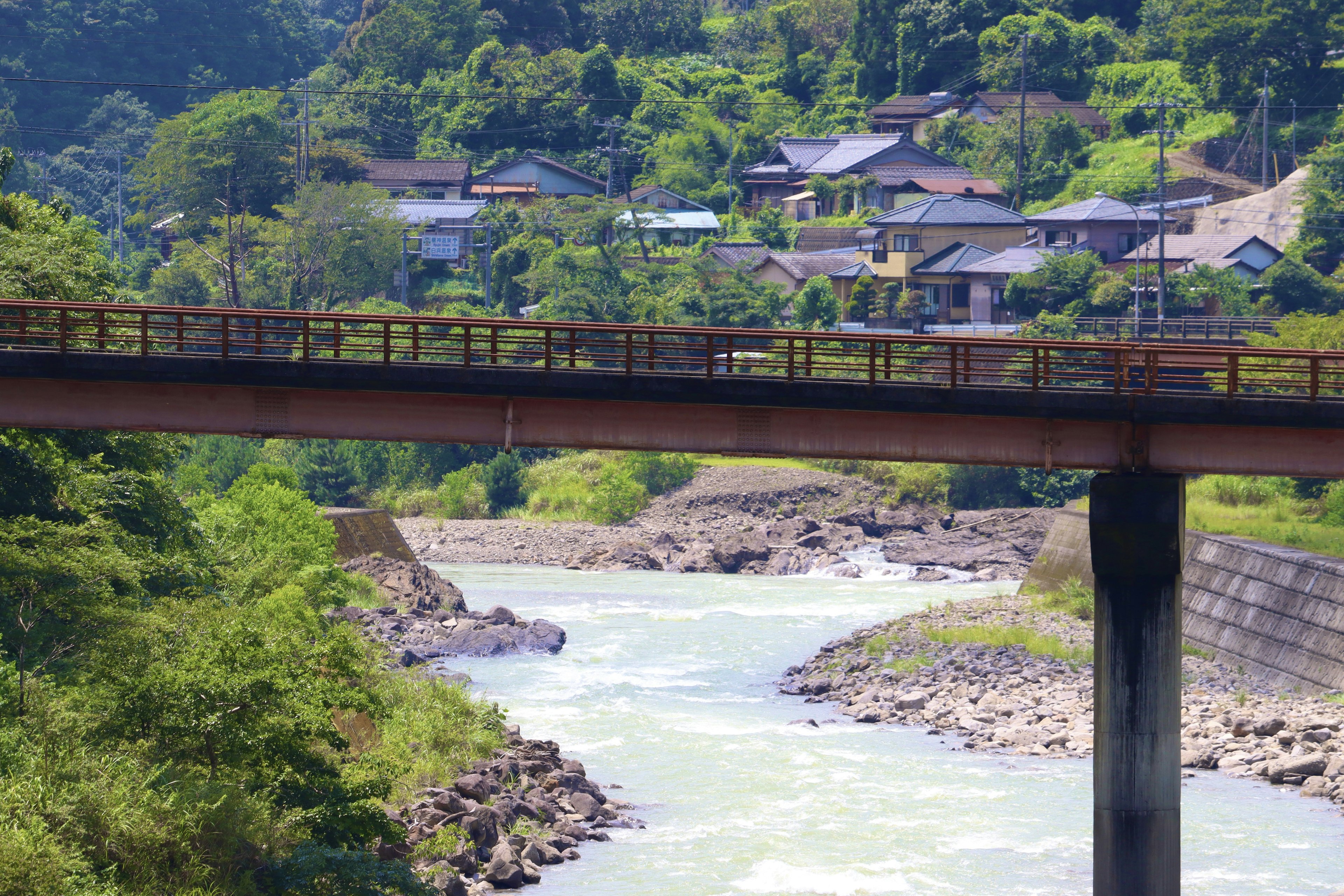 สะพานข้ามแม่น้ำพร้อมบ้านและภูเขาเขียวขจีในพื้นหลัง