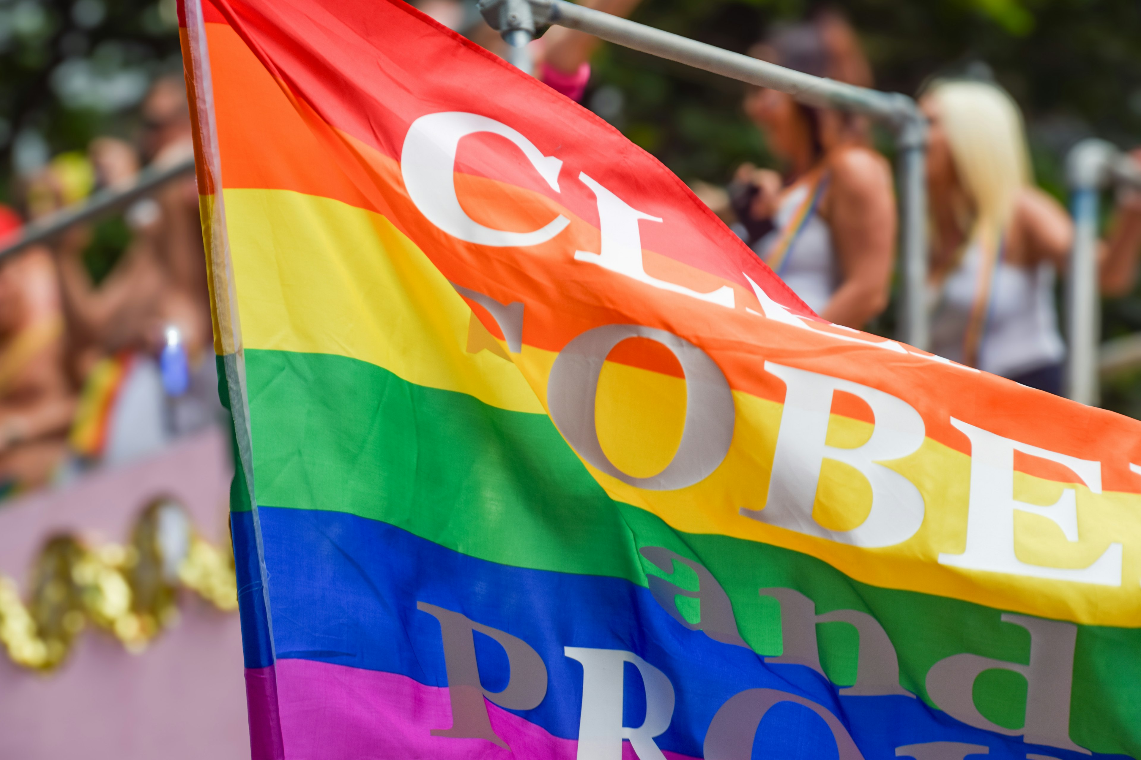 Eine Regenbogenflagge mit Text, die bei einer lebhaften Parade gehalten wird