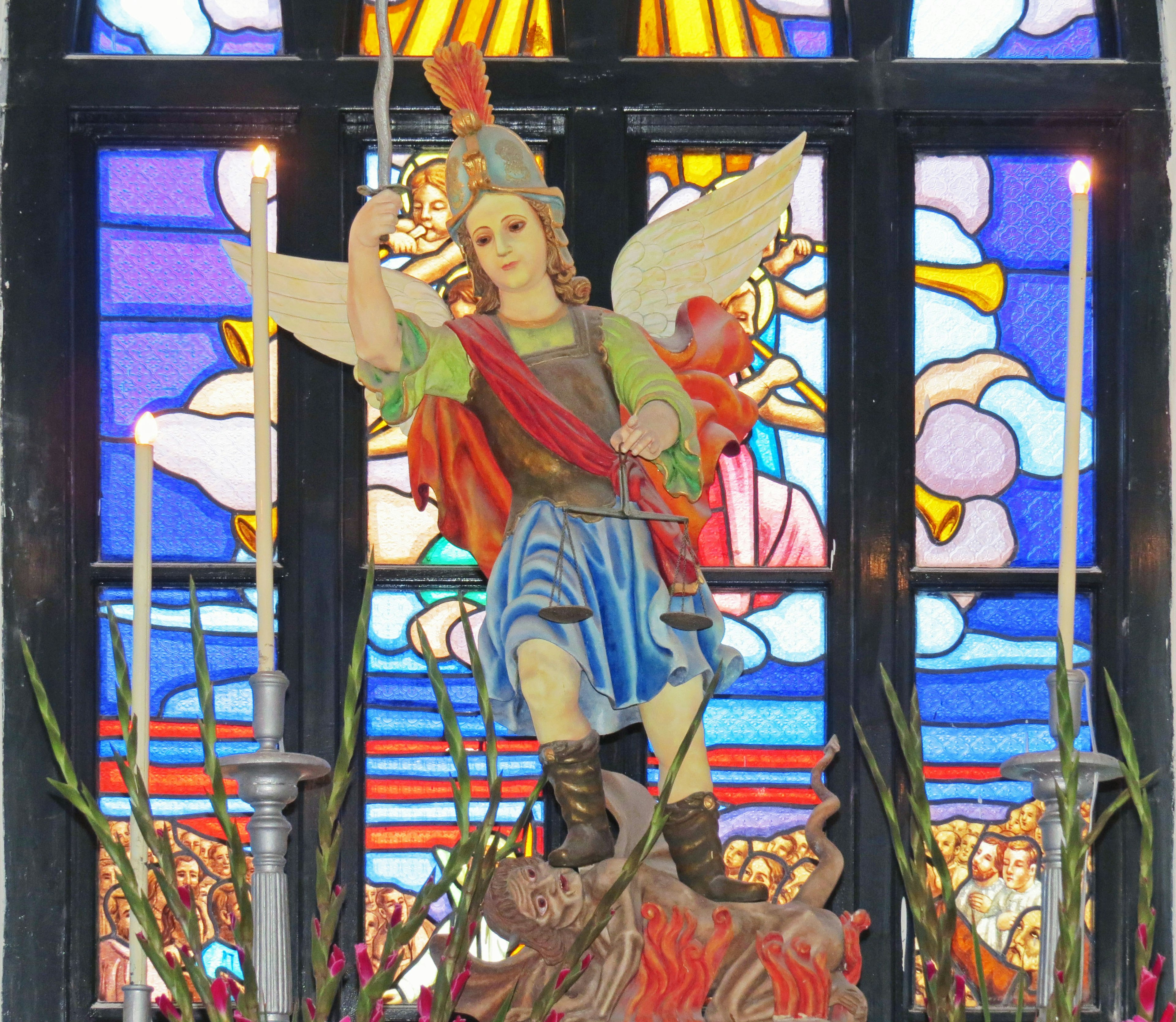 Statue of Saint Michael standing against a colorful stained glass background