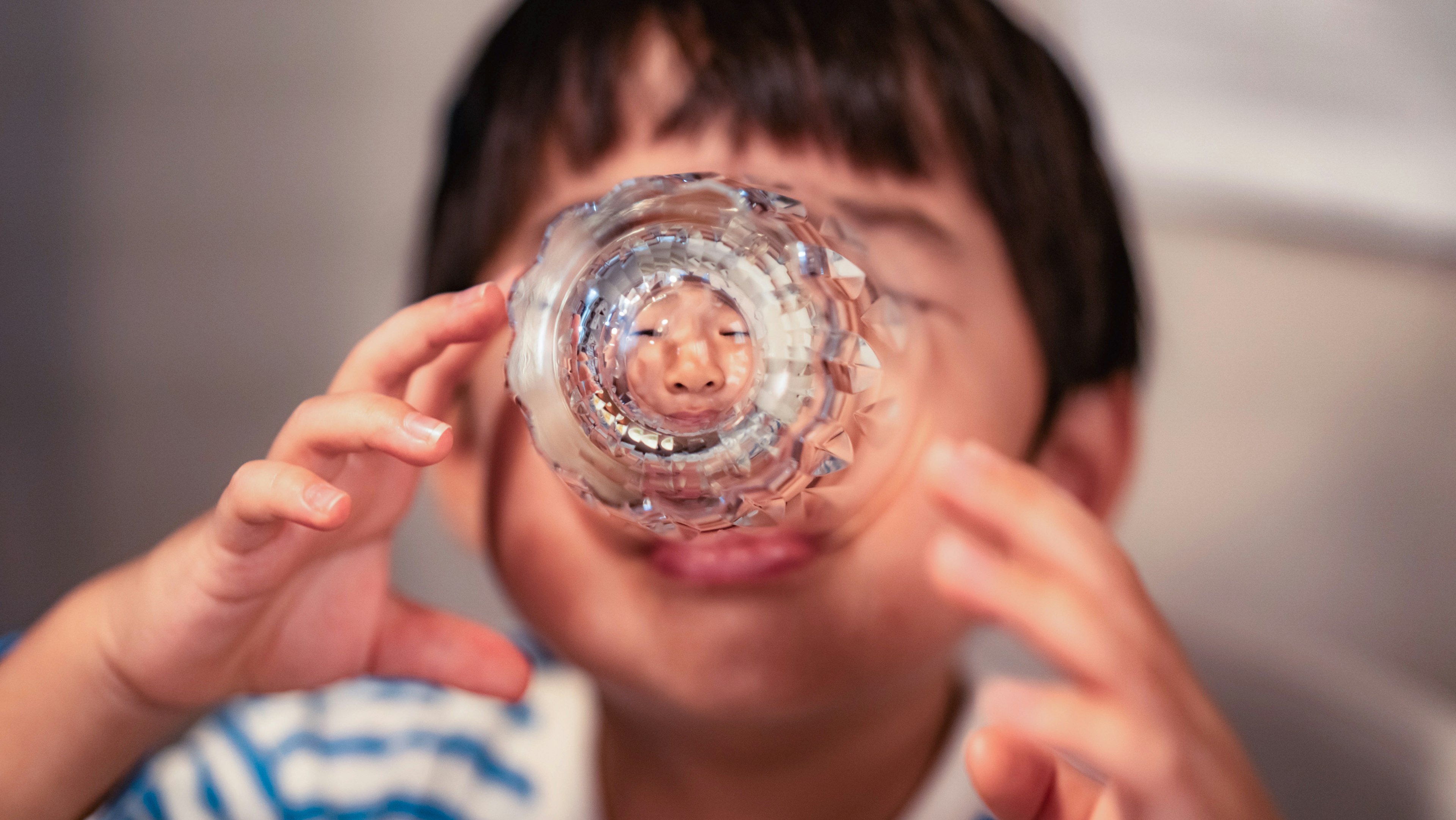 Niño mirando a través de un vaso transparente con una expresión juguetona