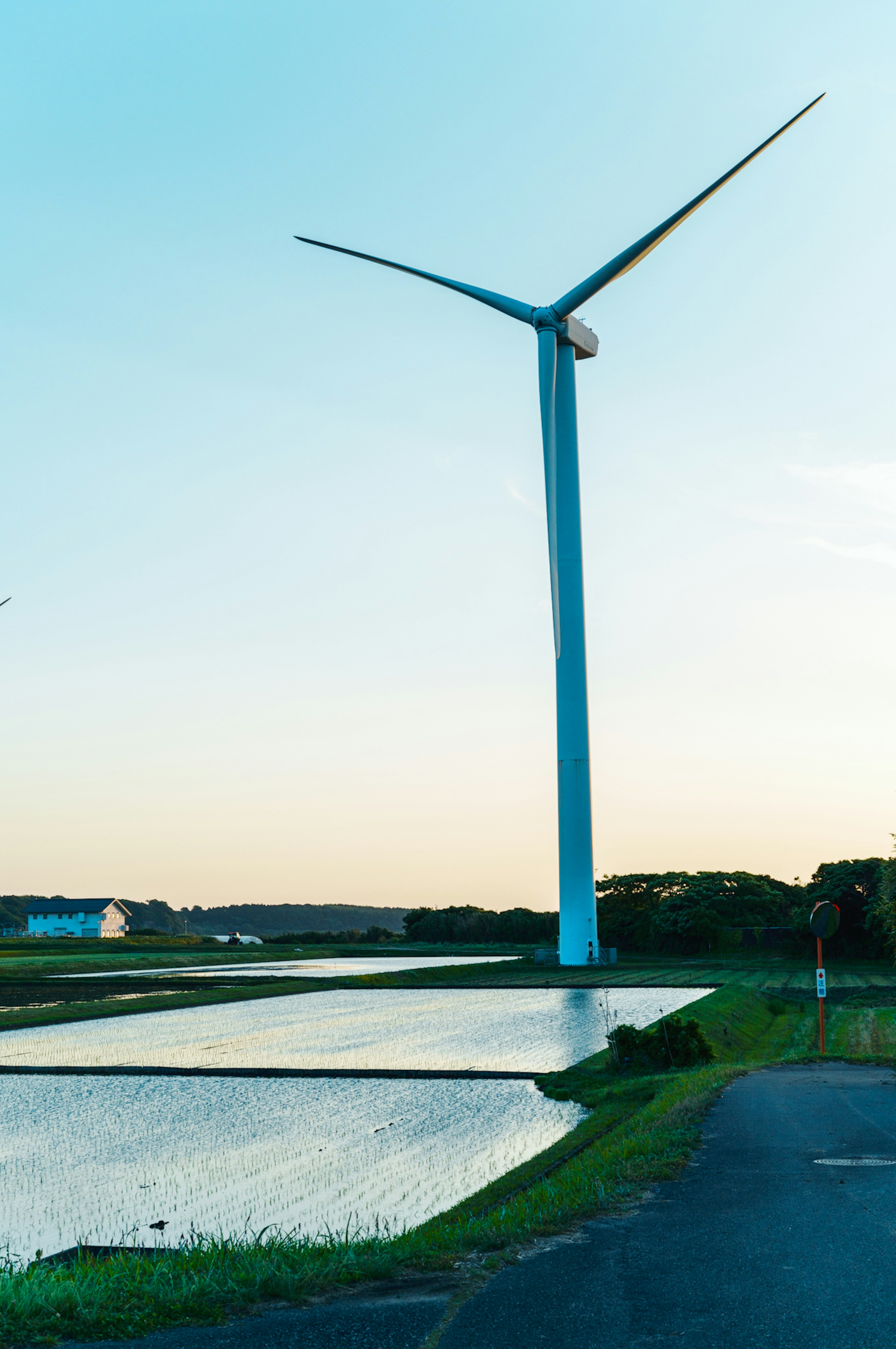 A wind turbine standing beside a calm body of water under a blue sky