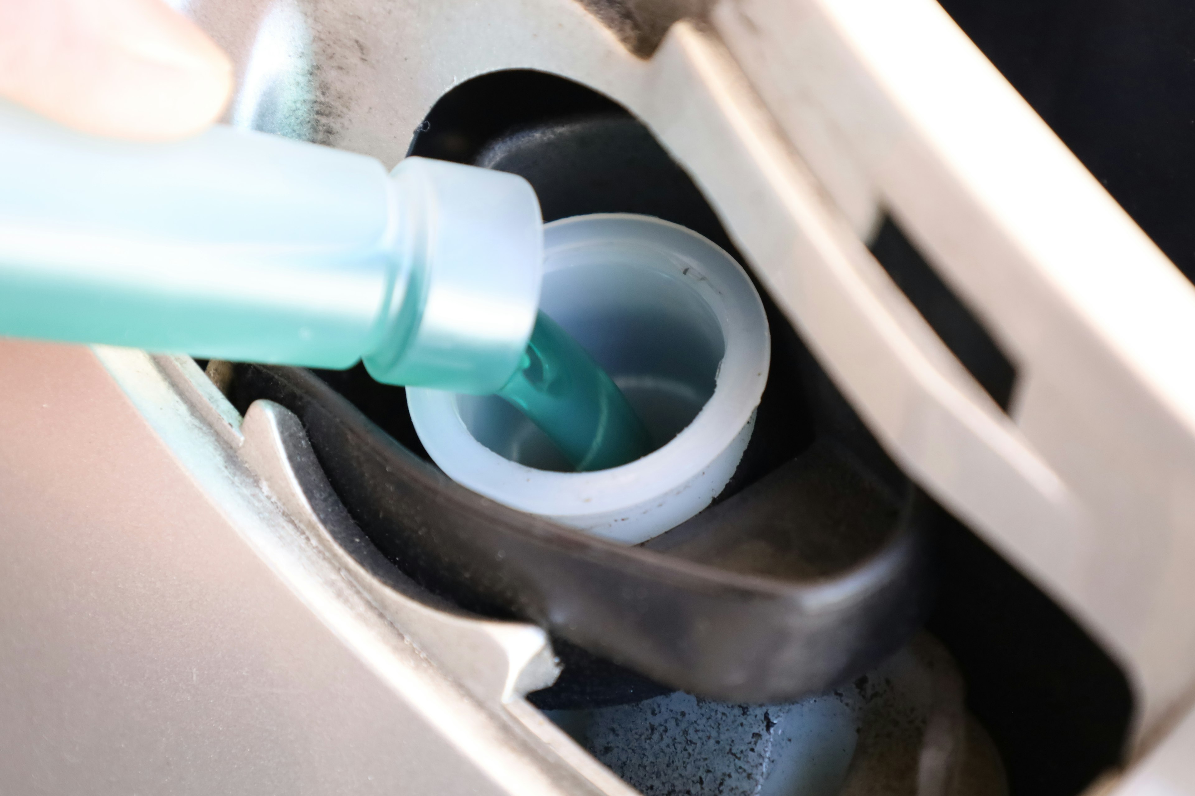 A hand pouring blue windshield washer fluid into a white reservoir