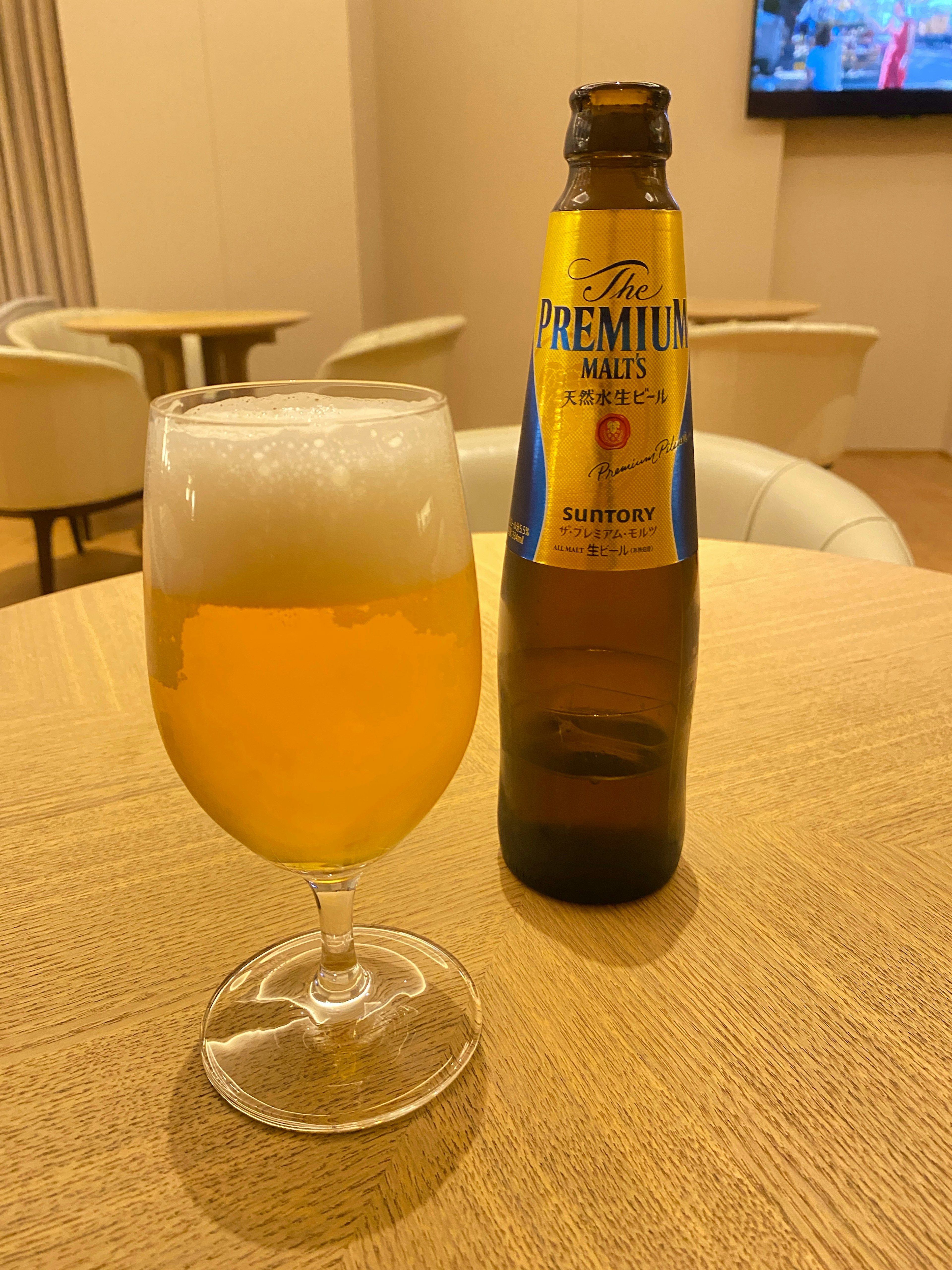 A glass of beer with foam and a bottle on a wooden table