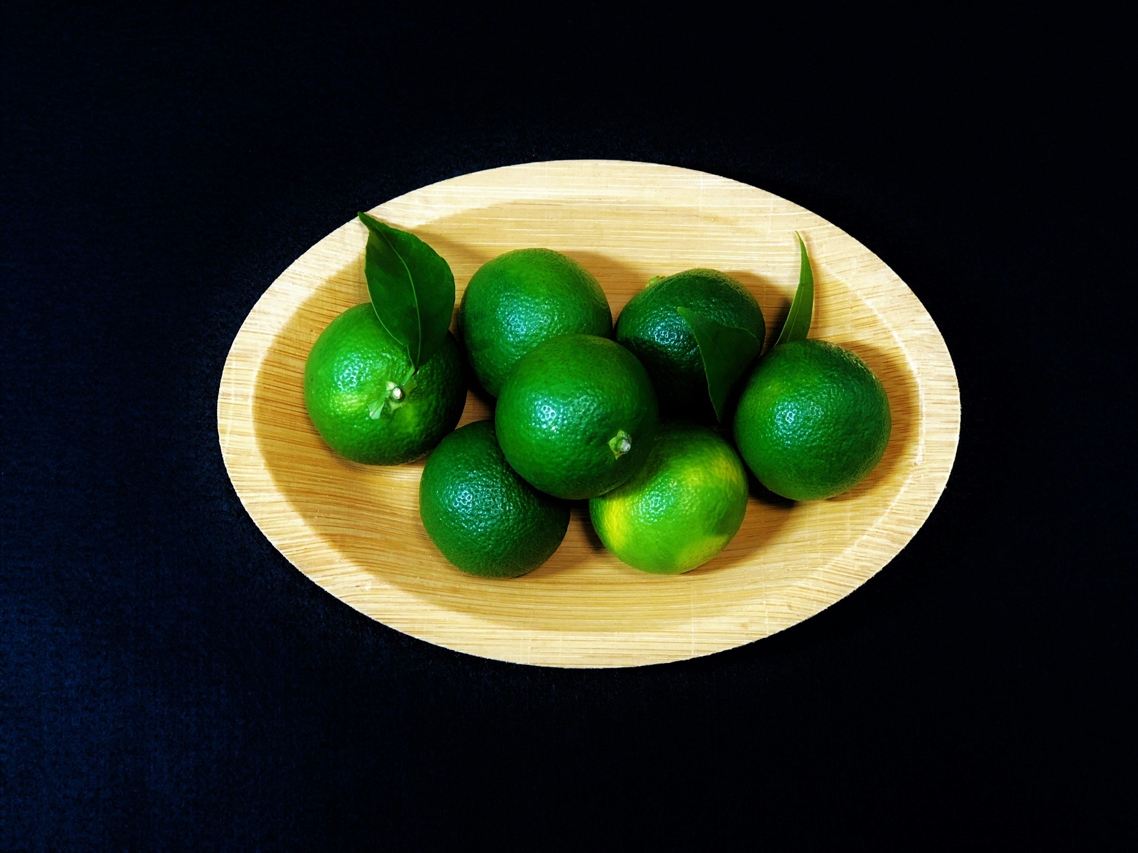 Limones verdes con hojas en un cuenco de madera