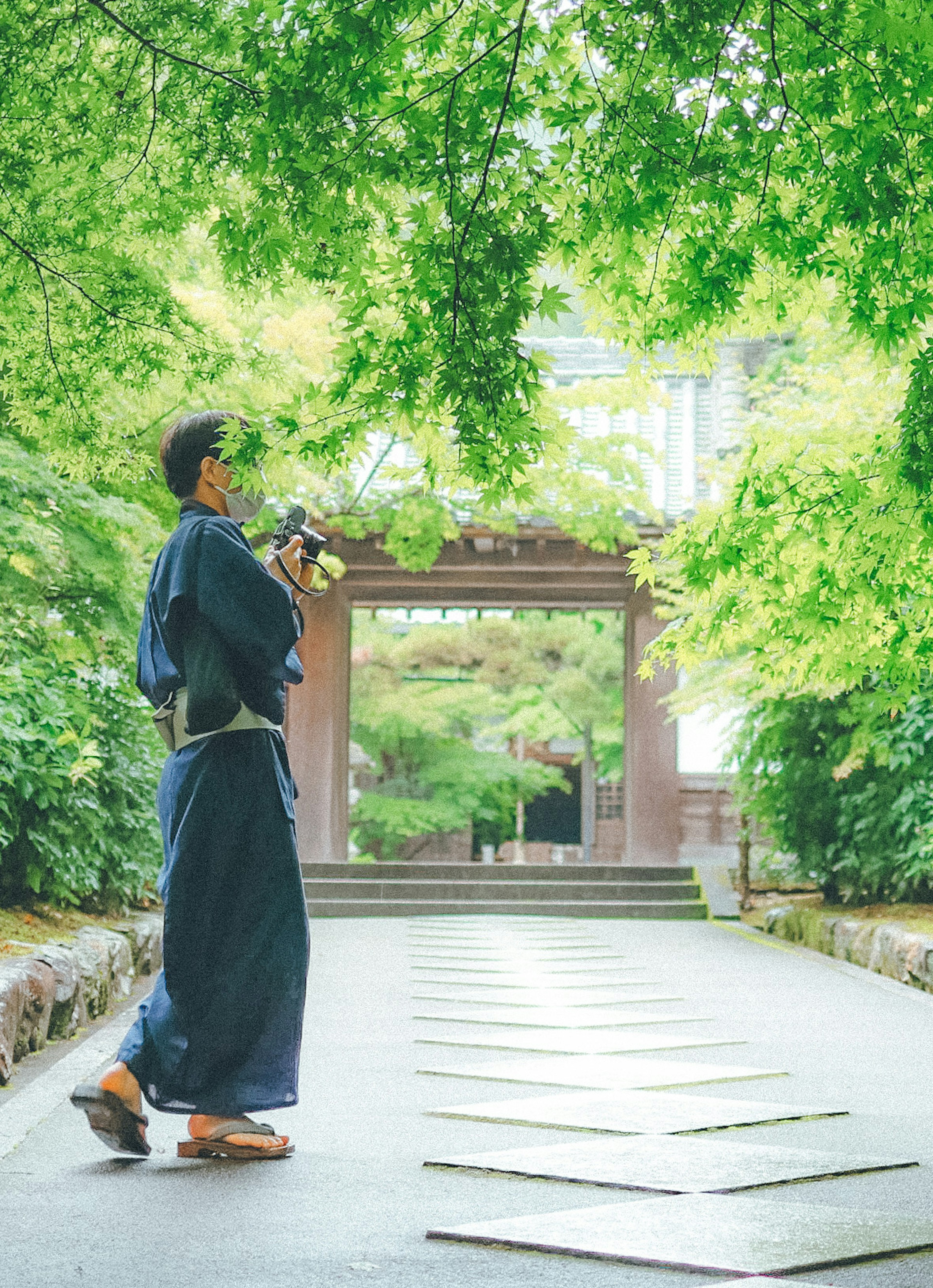 緑豊かな庭園の中で着物を着た男性が立っている