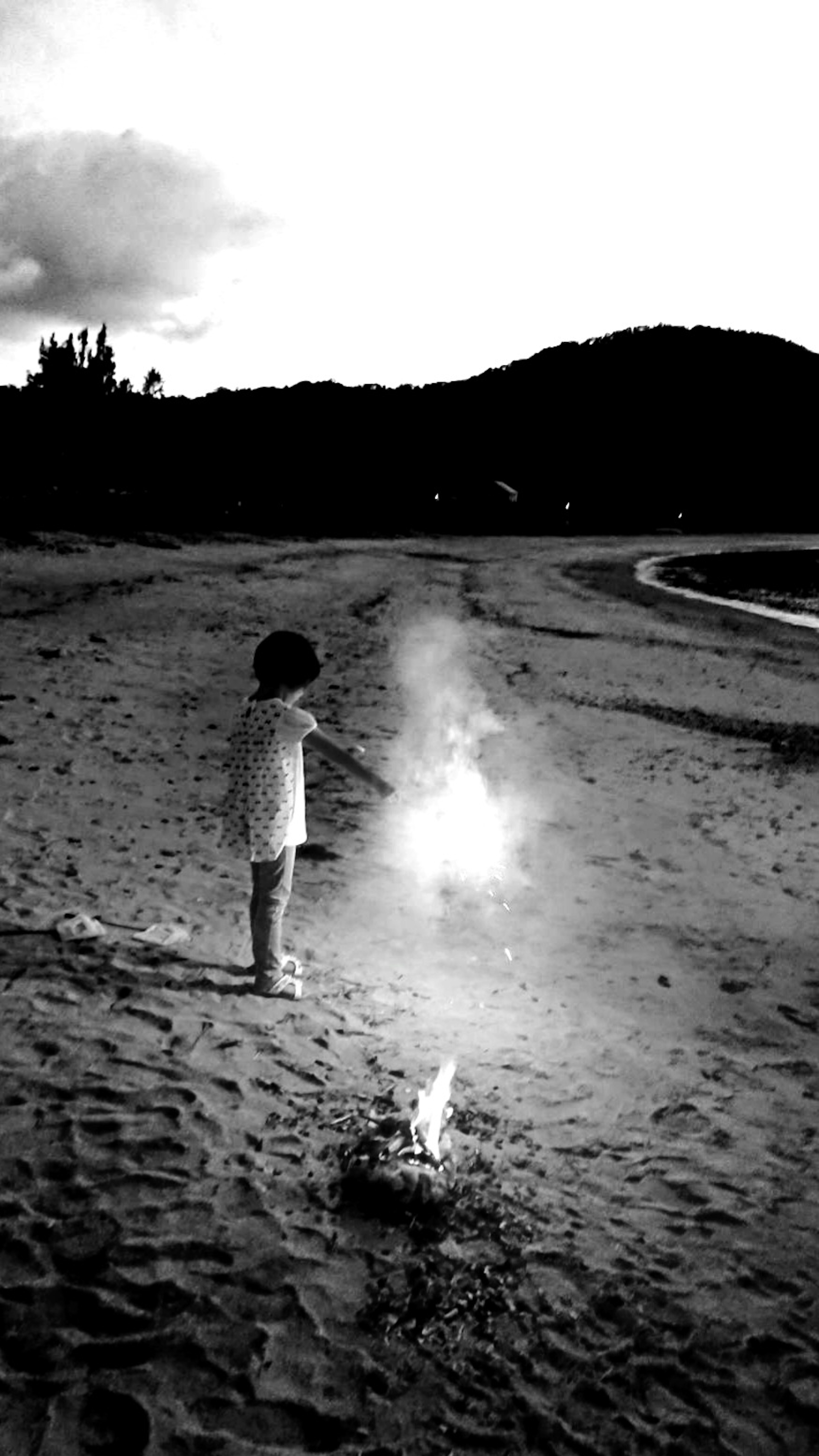 Foto in bianco e nero di un bambino che tiene fuochi d'artificio sulla spiaggia