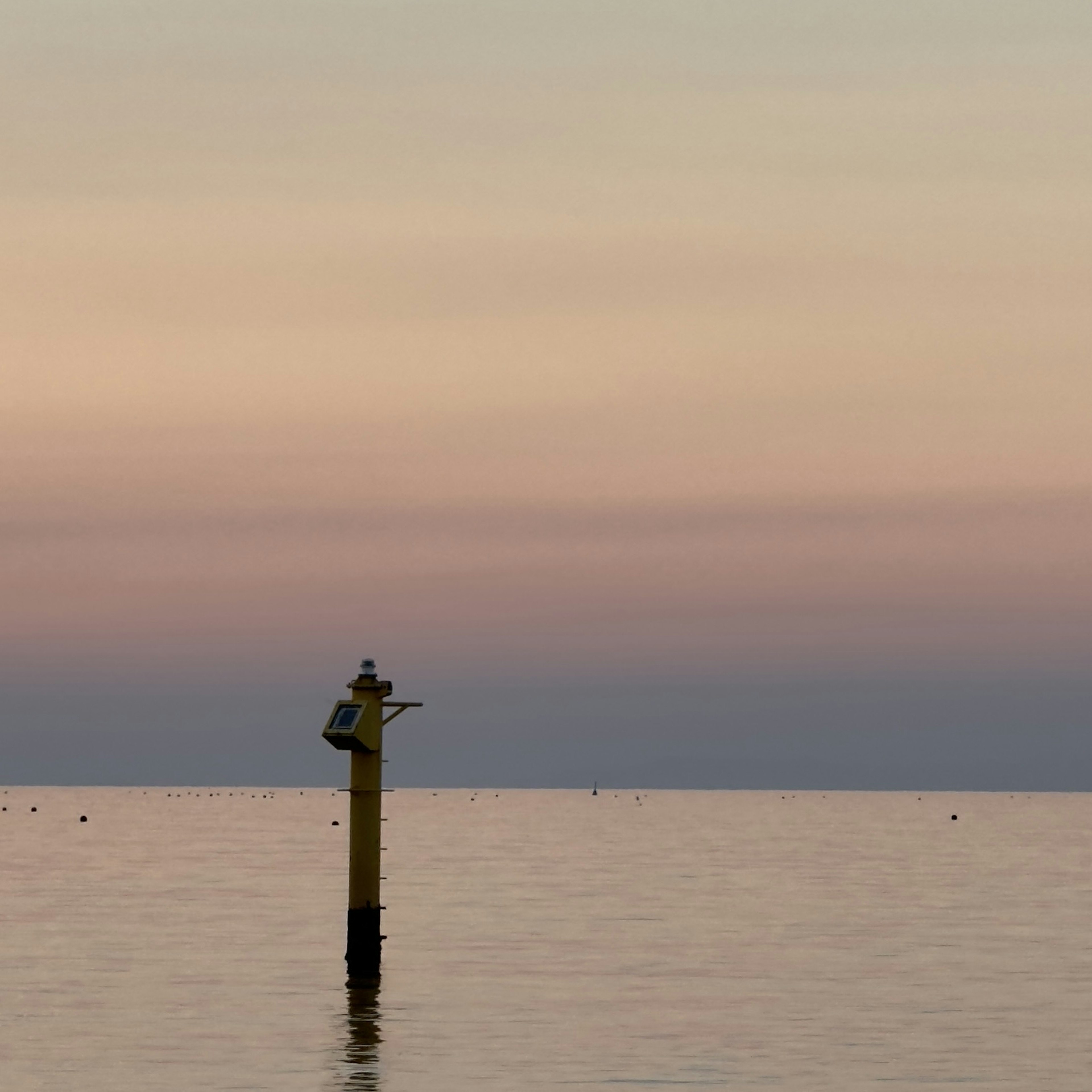 Vue panoramique de la mer calme avec un ciel pastel et un poteau de balisage jaune