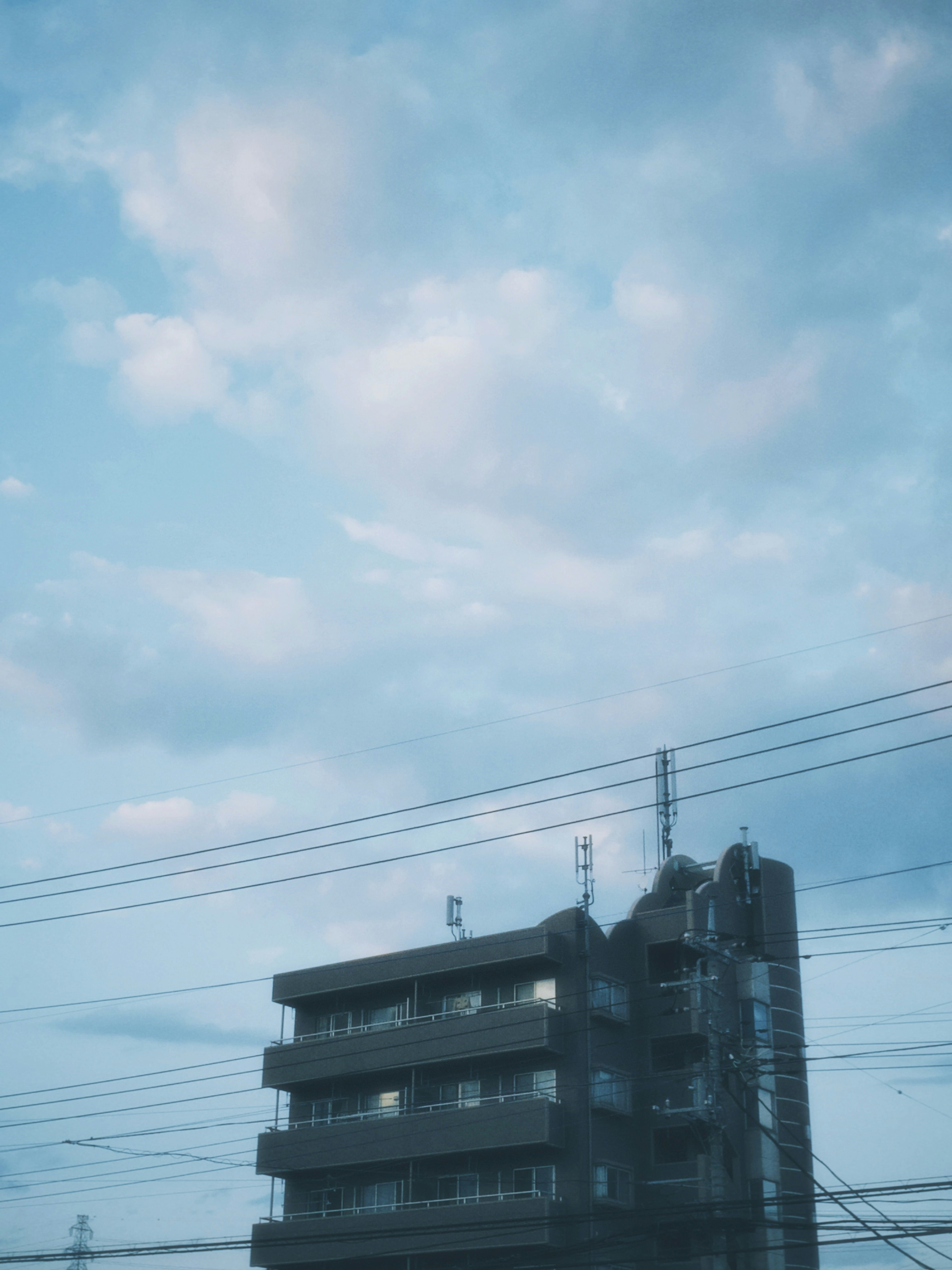 青空と雲を背景にしたビルの写真で電線が見える