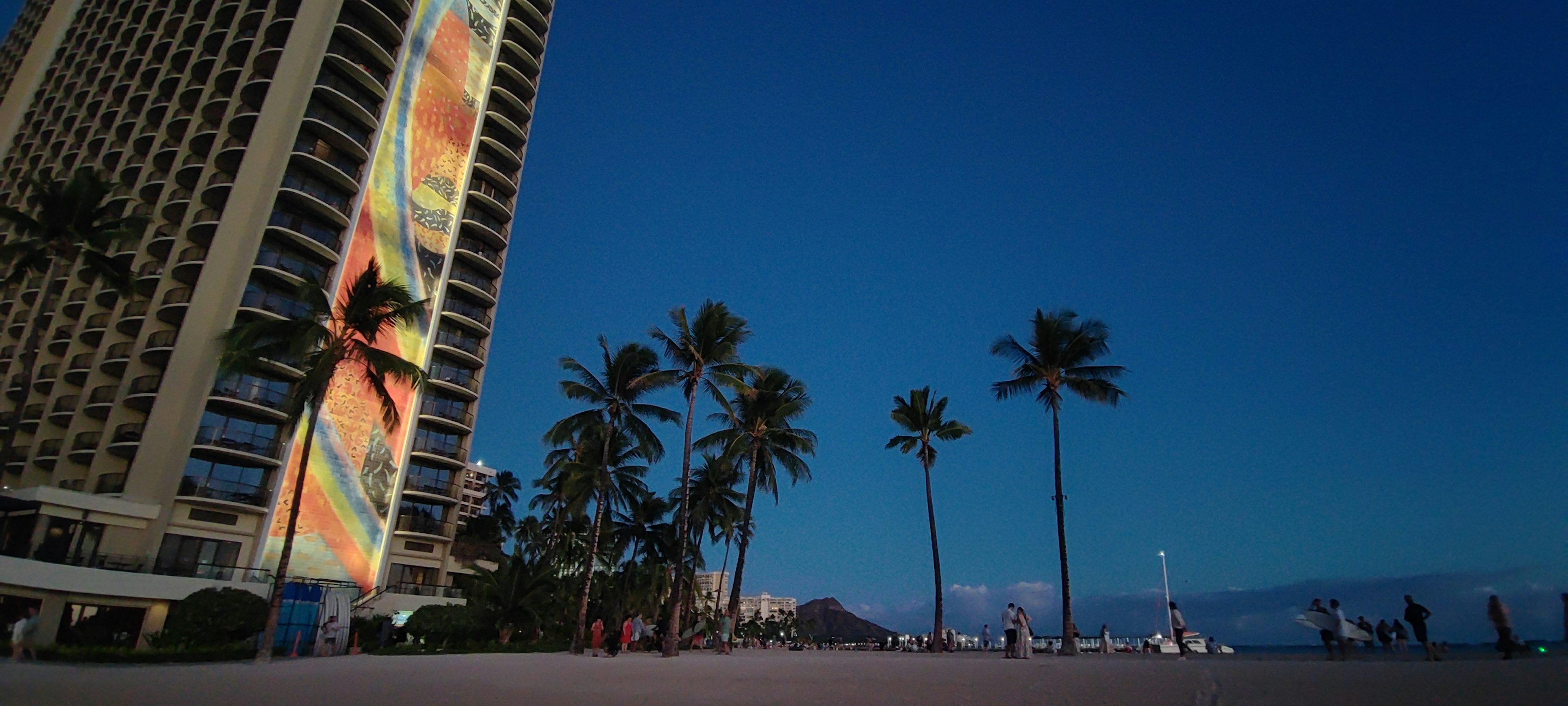 Tall building by the beach illuminated with colorful art under the night sky