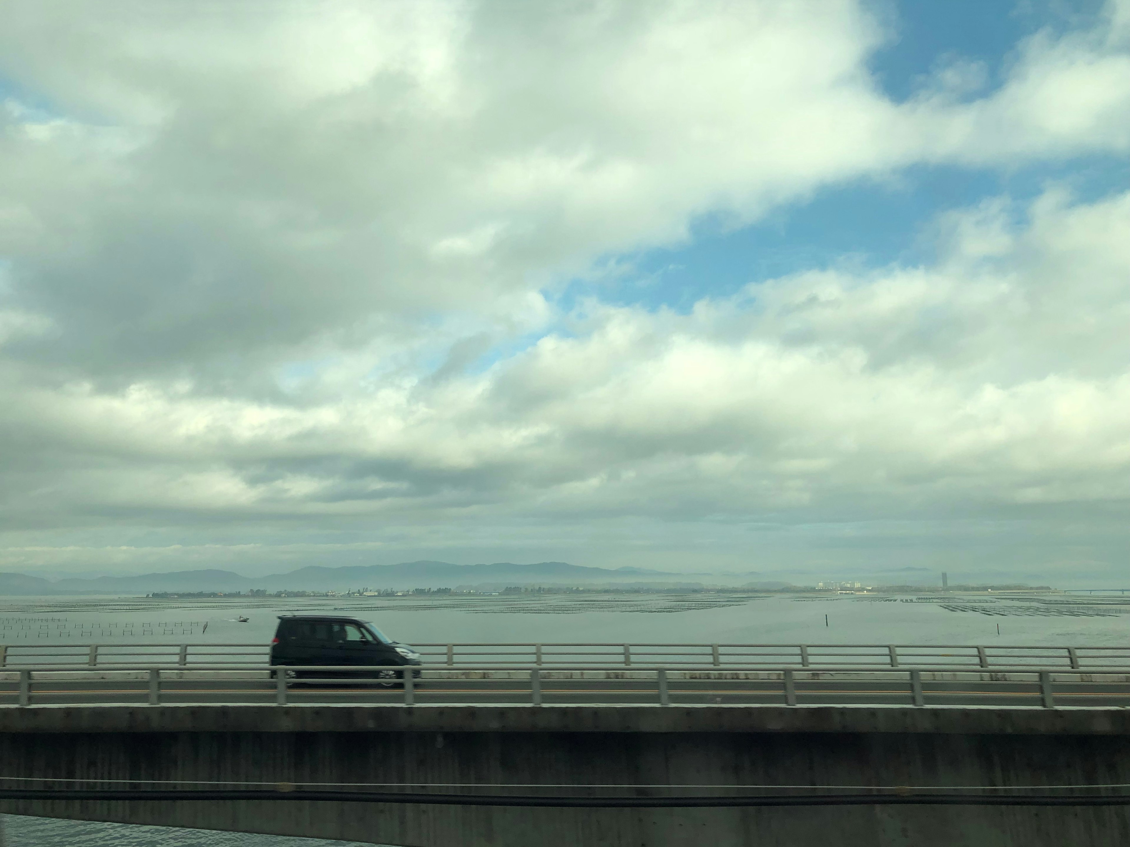 青い空と雲の下を走る黒いバンと広がる海