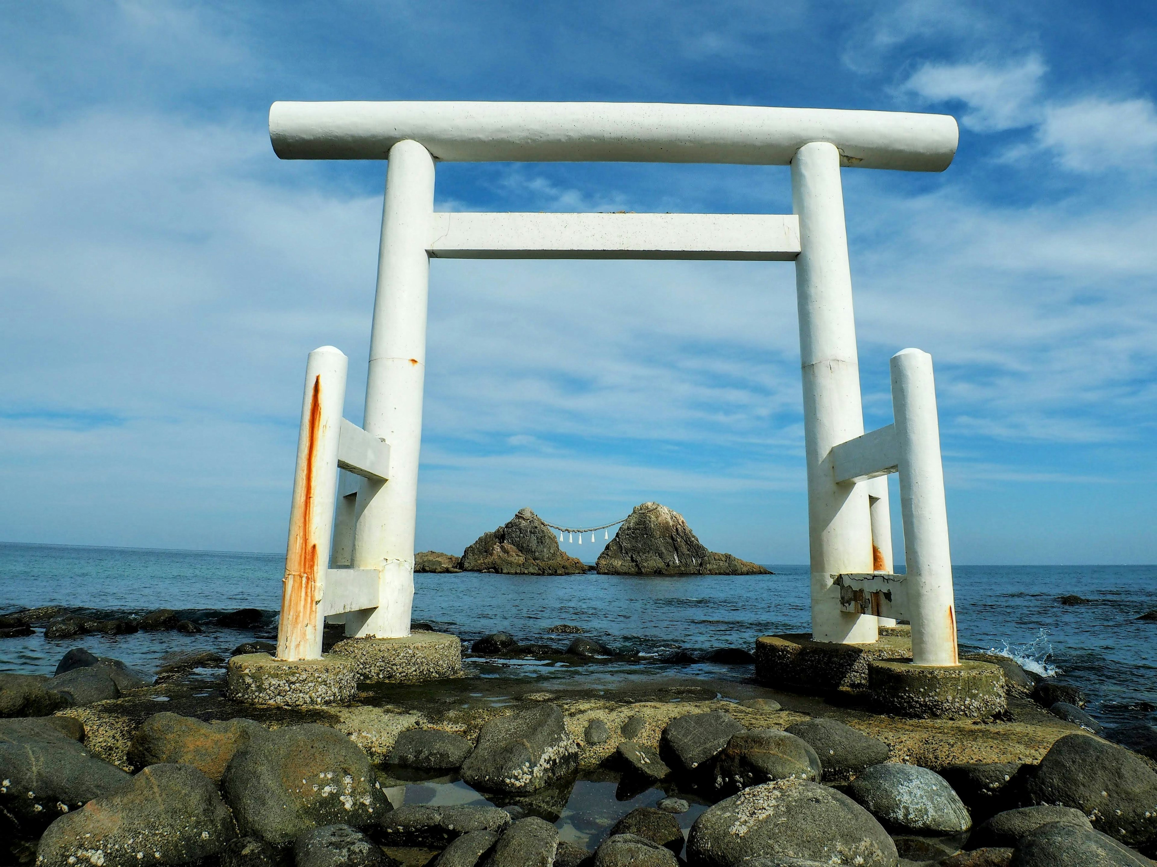 Cổng torii trắng gần biển với bờ đá