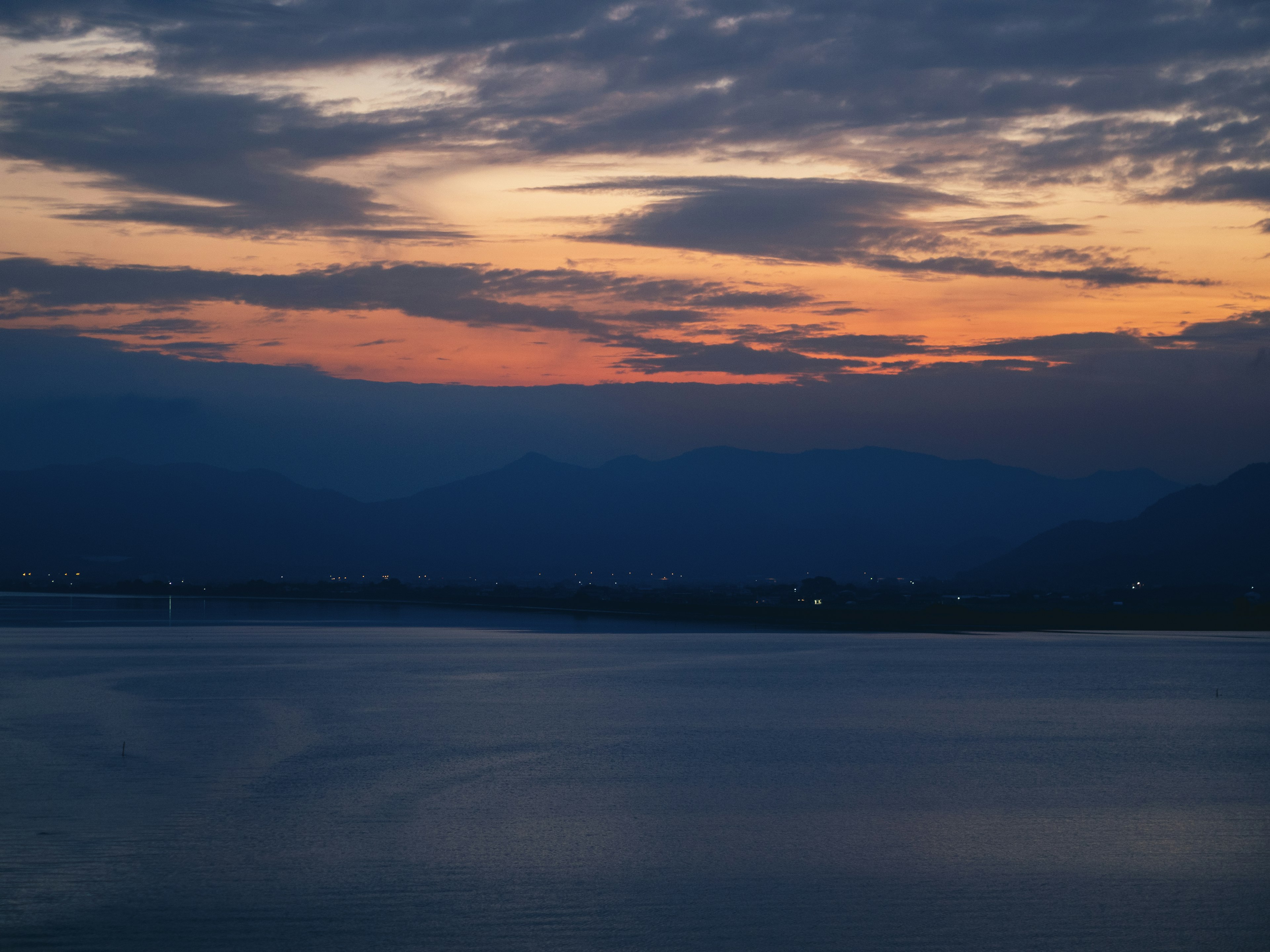 Tramonto su un lago calmo con montagne in lontananza