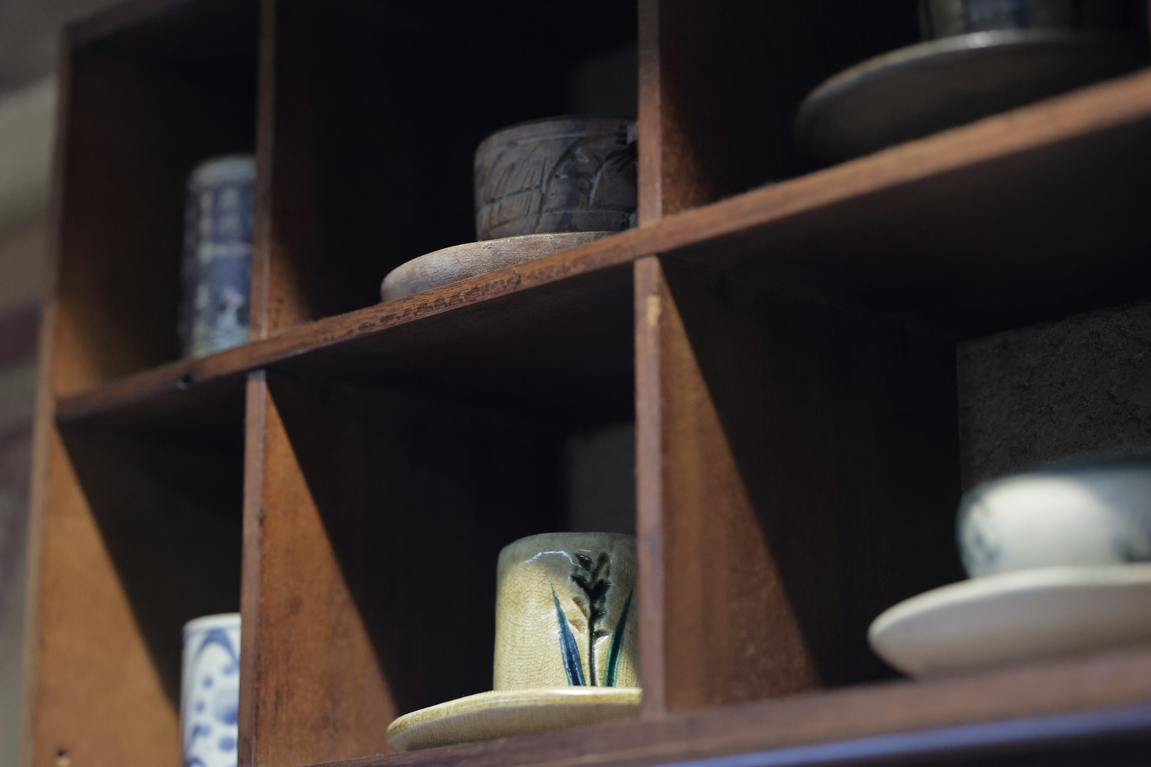 Exhibición de varias tazas de té y platos en una estantería de madera