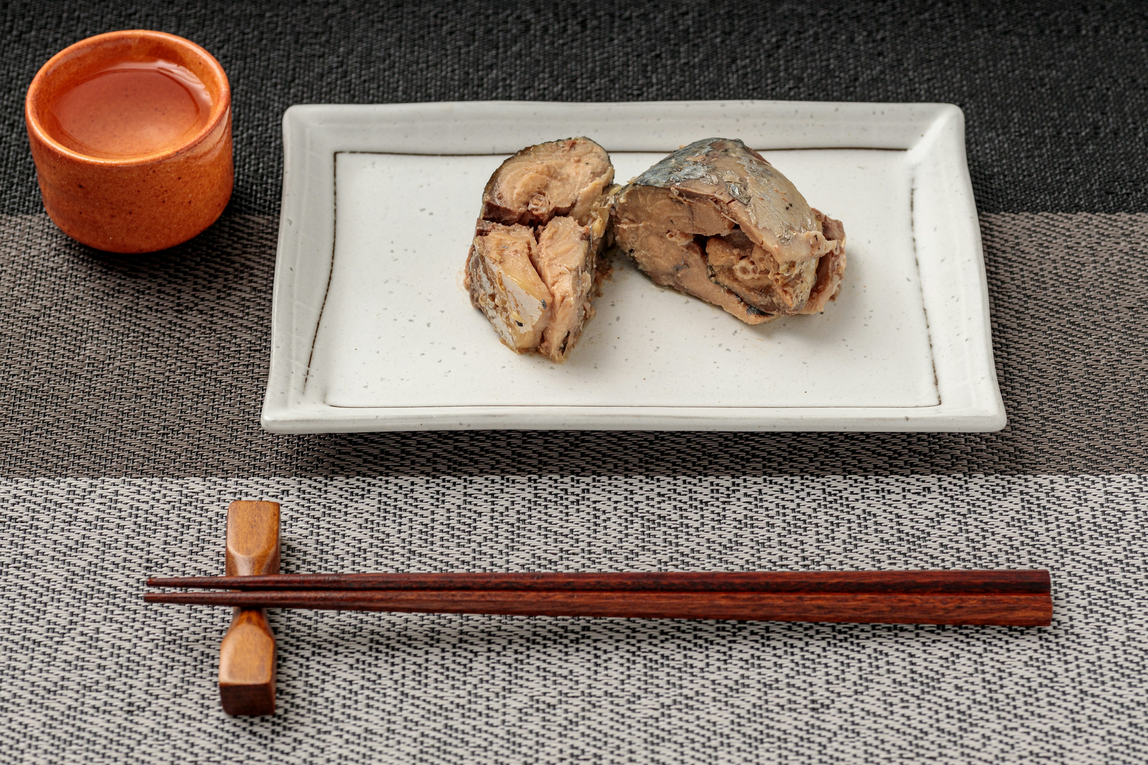 Cooked fish fillets on a white plate with a small orange cup of drink nearby