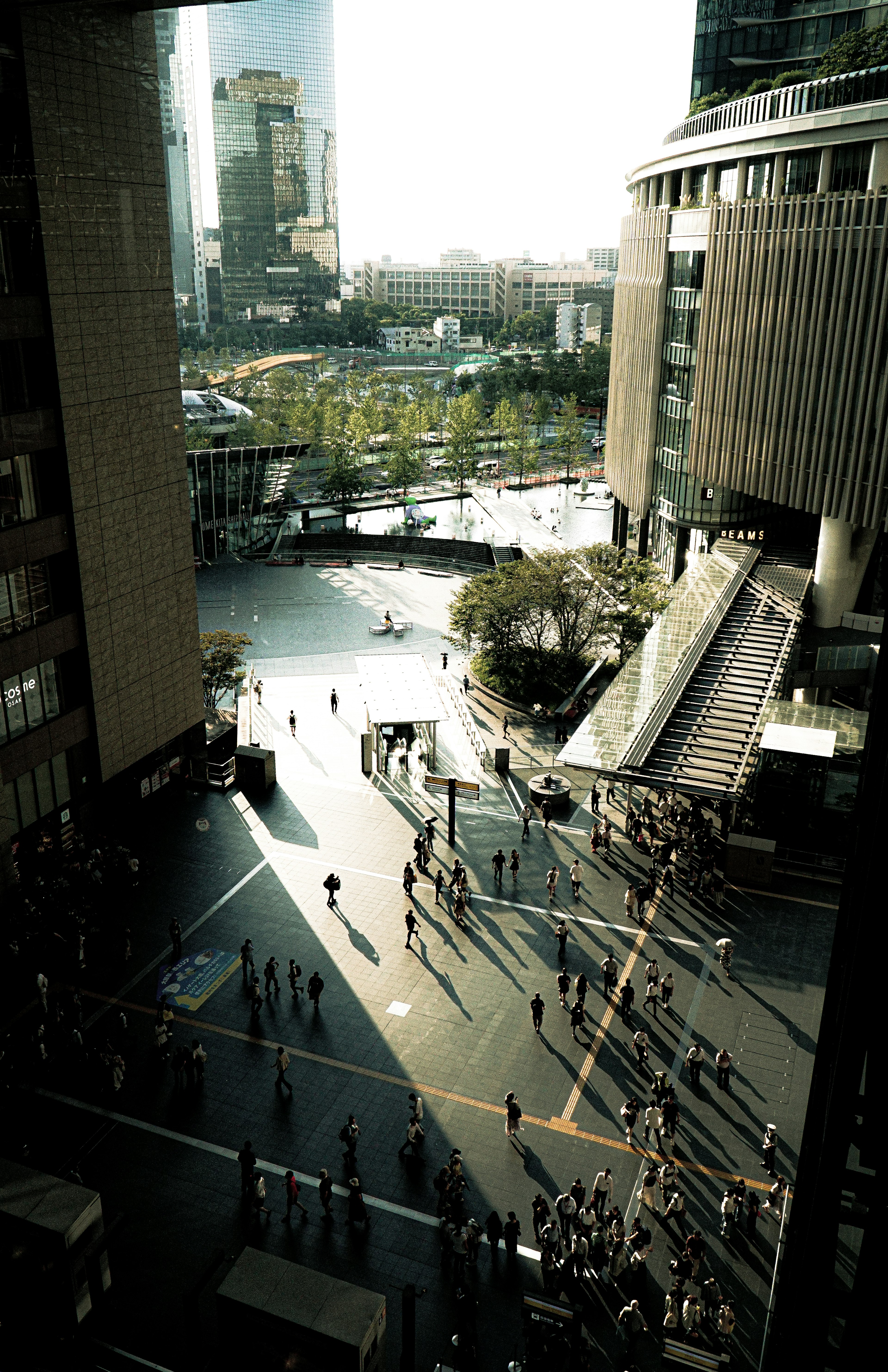 A busy plaza between buildings with pedestrians and greenery