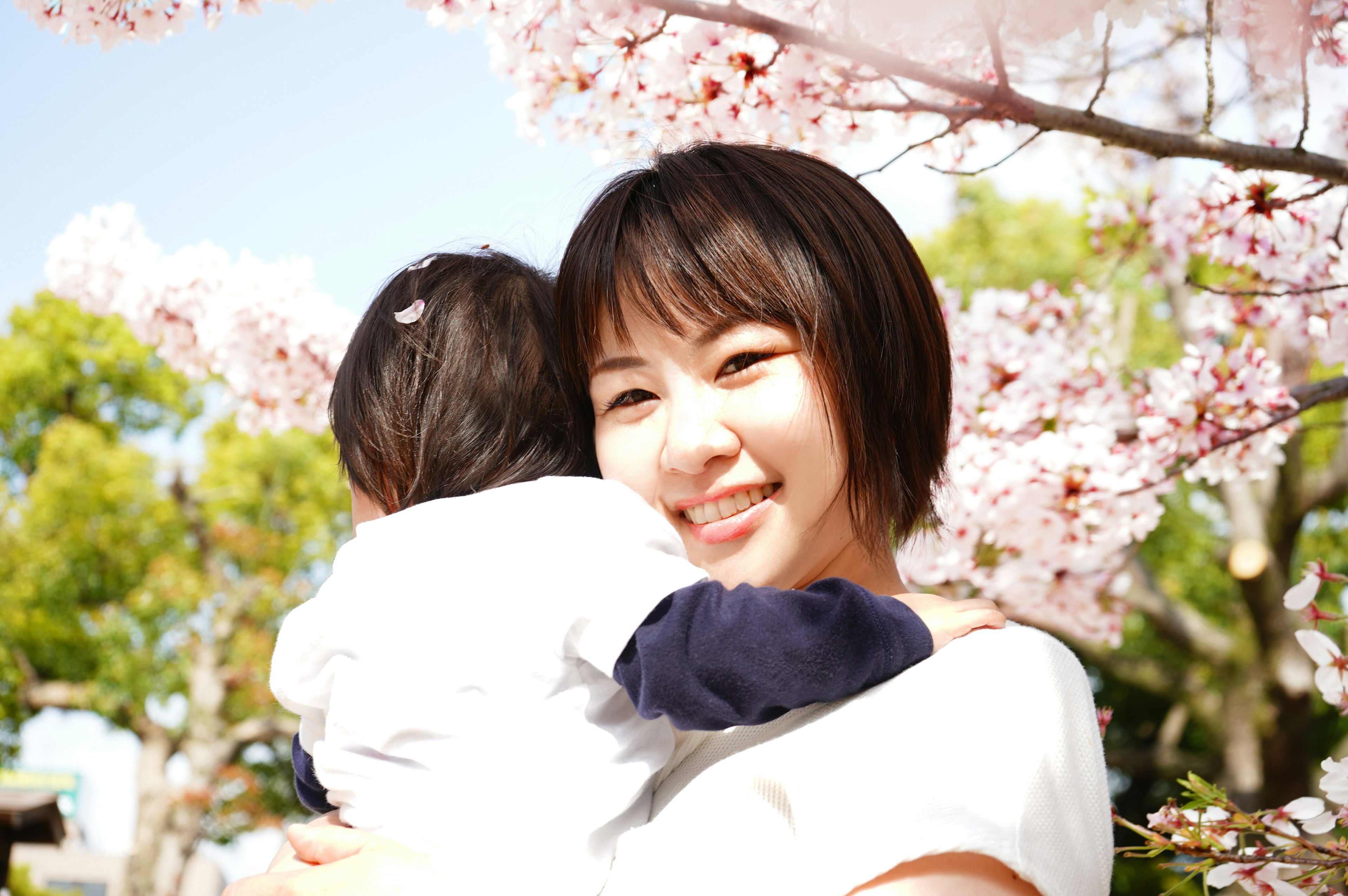 Smiling woman holding a child under cherry blossom trees