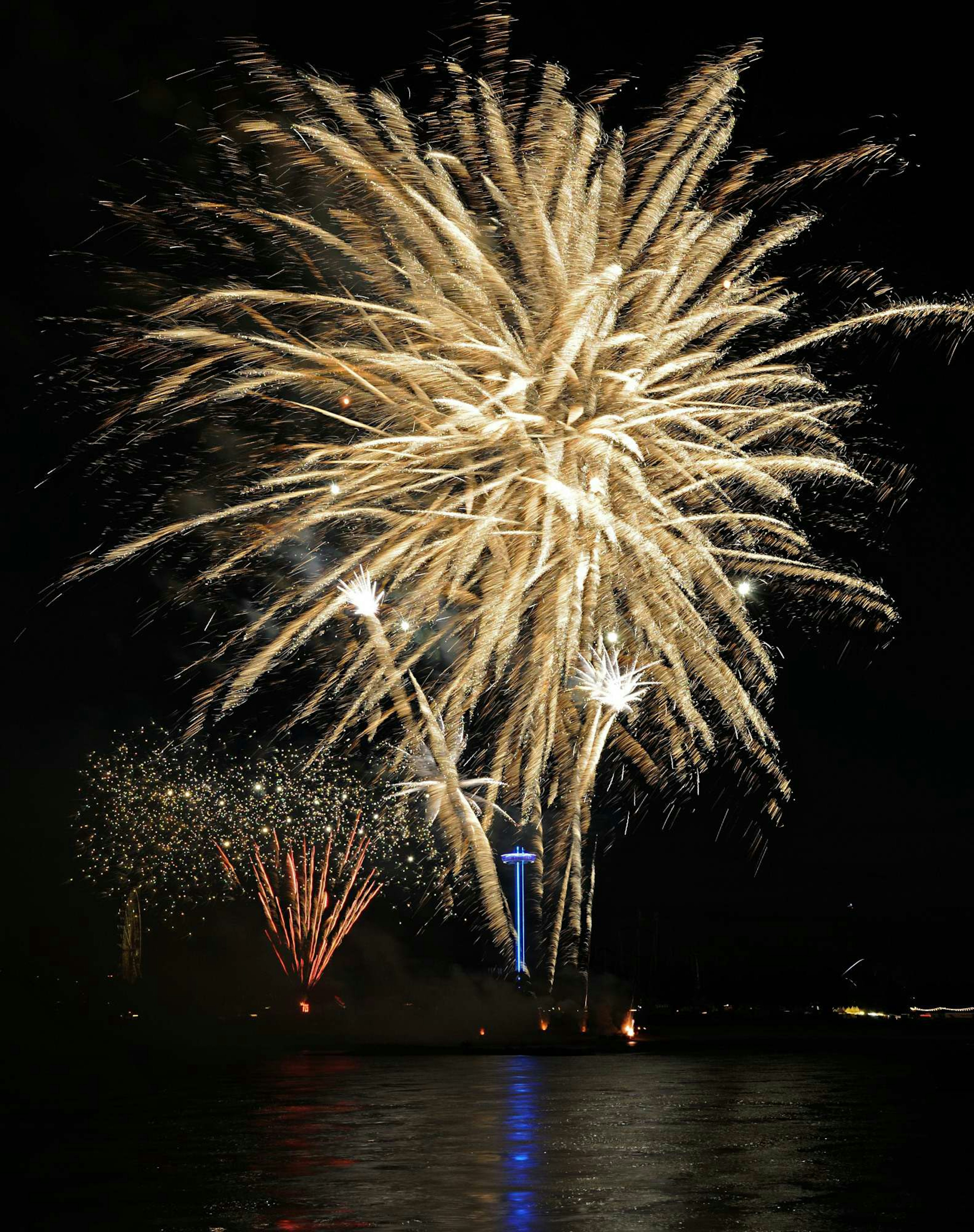 A vibrant display of large fireworks bursting in the night sky with smaller fireworks in the background