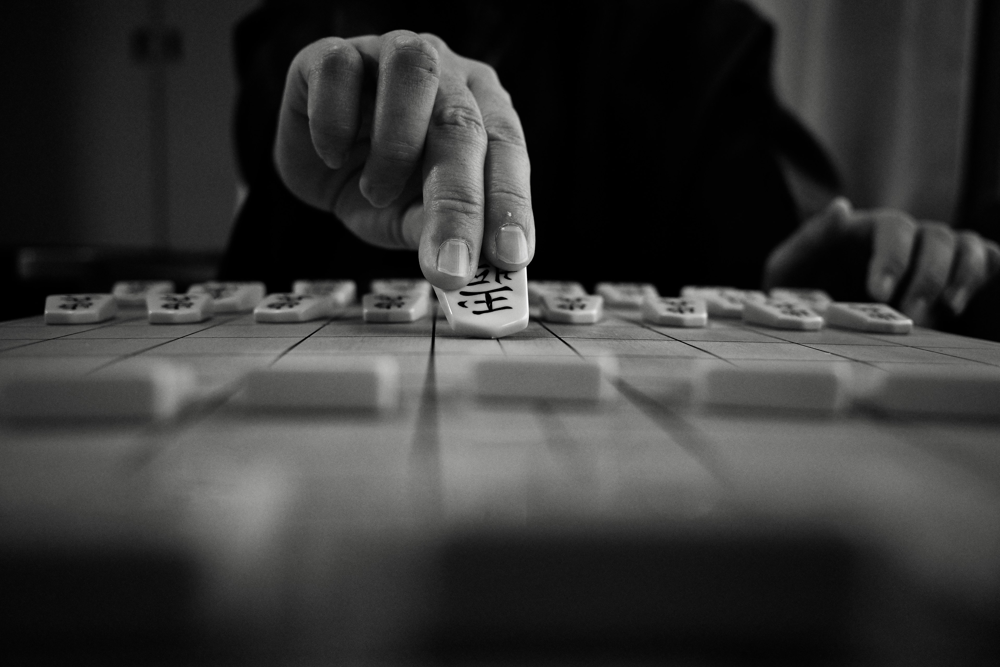 Một bàn tay đặt quân bài Mahjong lên bàn chơi trong ảnh đen trắng