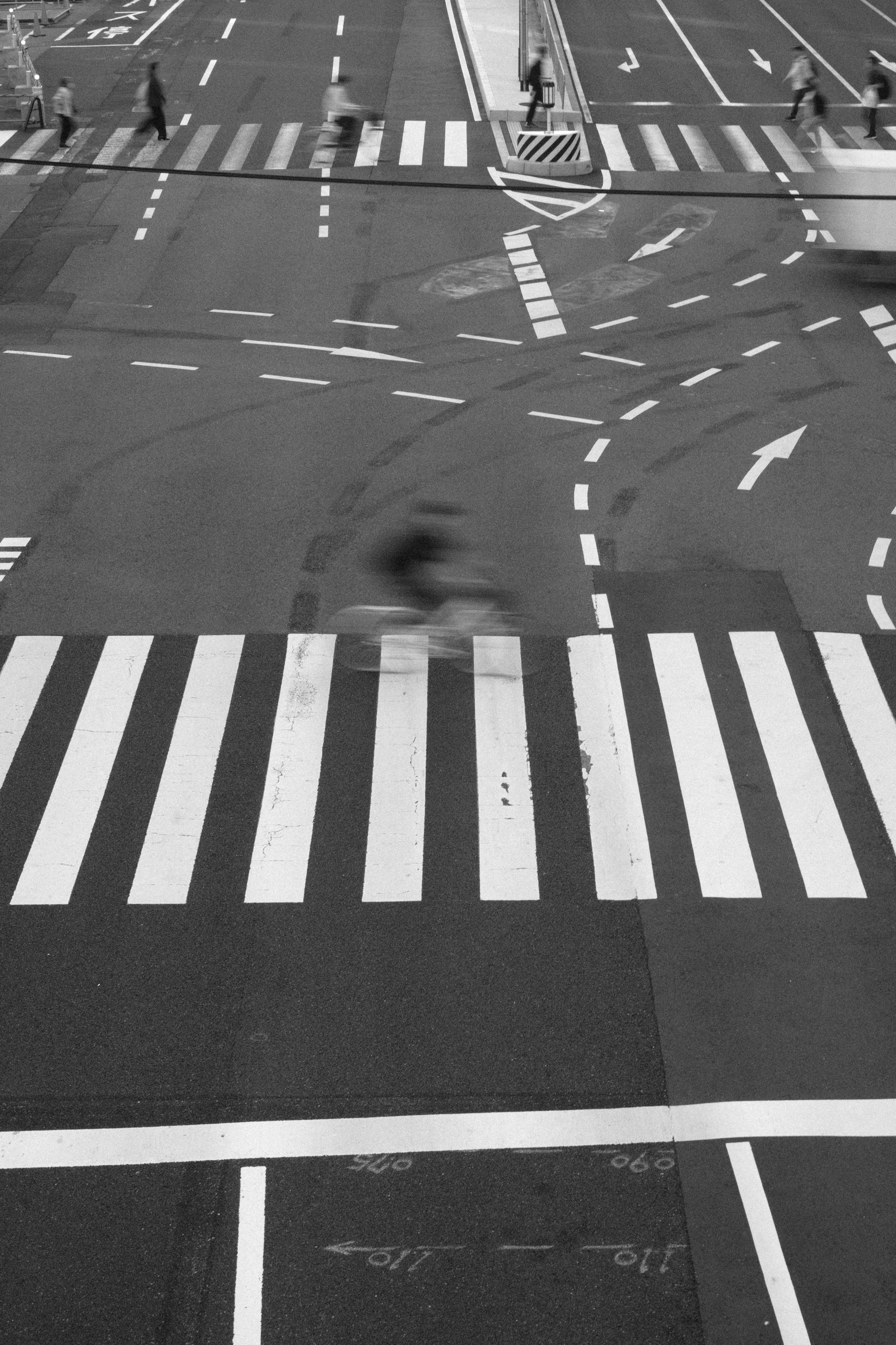 Black and white image of an intersection featuring striped crosswalks and traffic movement