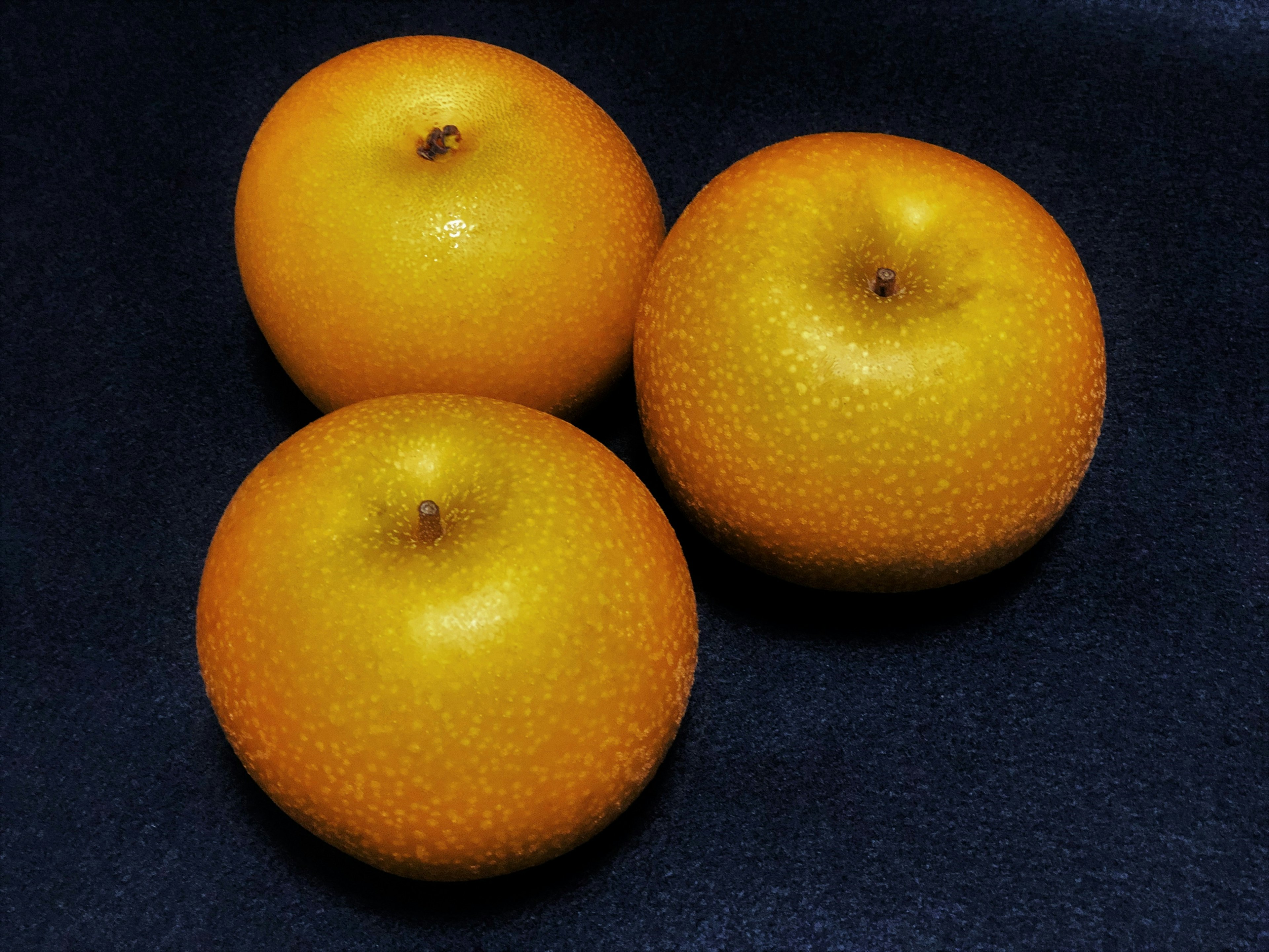 Tres frutas naranjas dispuestas sobre un fondo negro