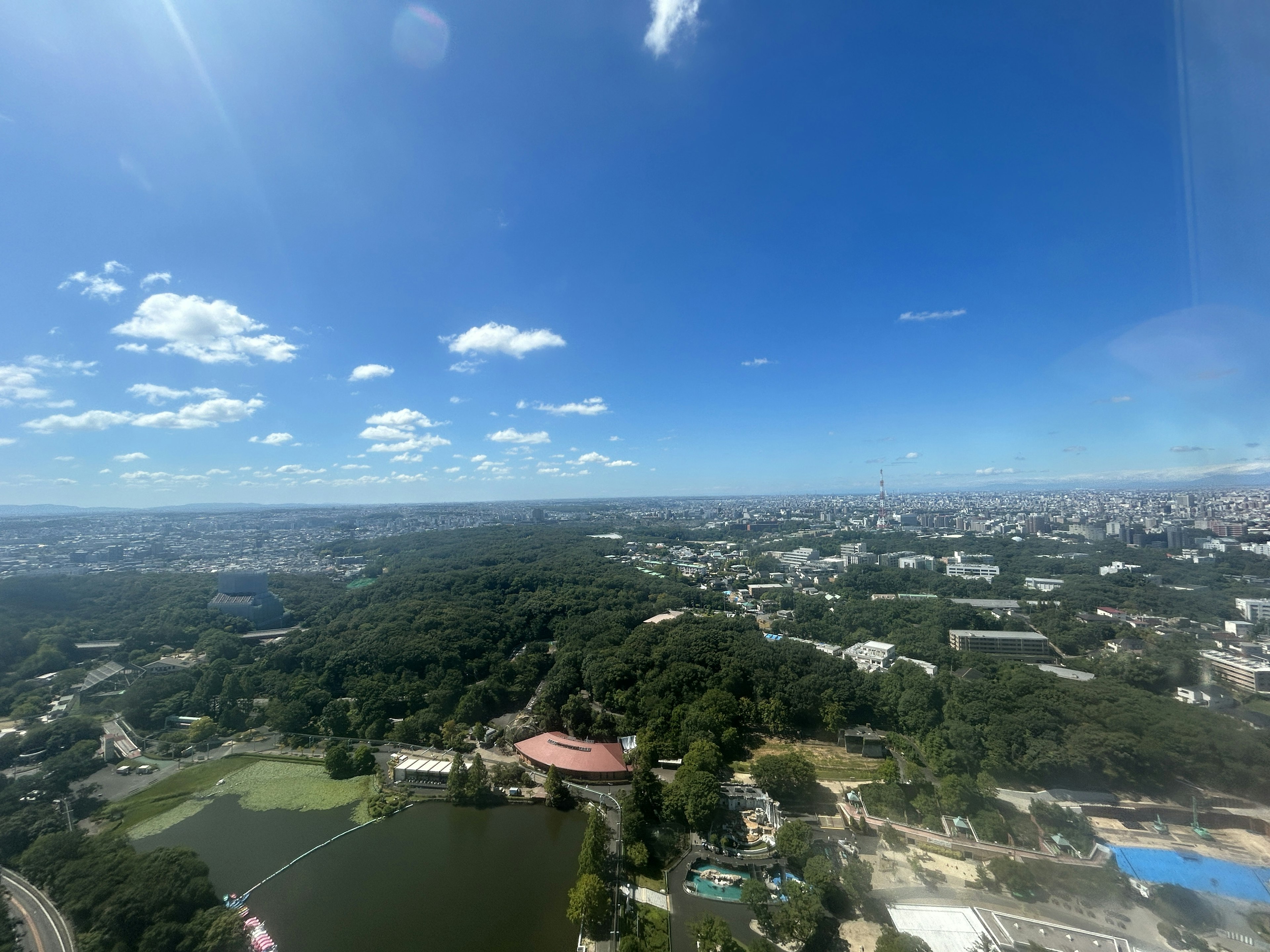 从高楼大厦俯瞰一座广阔城市的全景，蓝天与白云相映，公园和池塘清晰可见