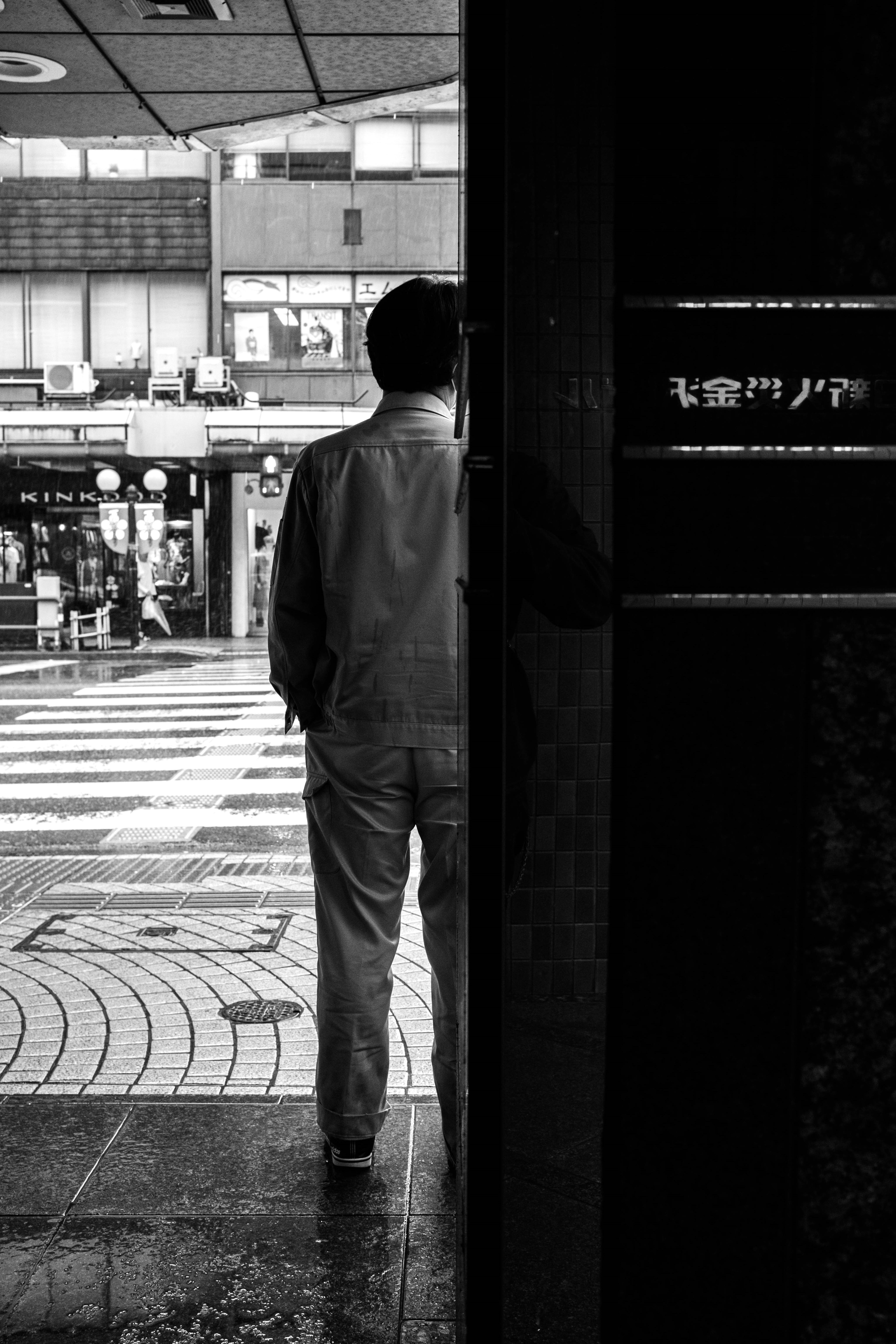 Un homme debout à un coin de rue en noir et blanc avec un sol mouillé par la pluie