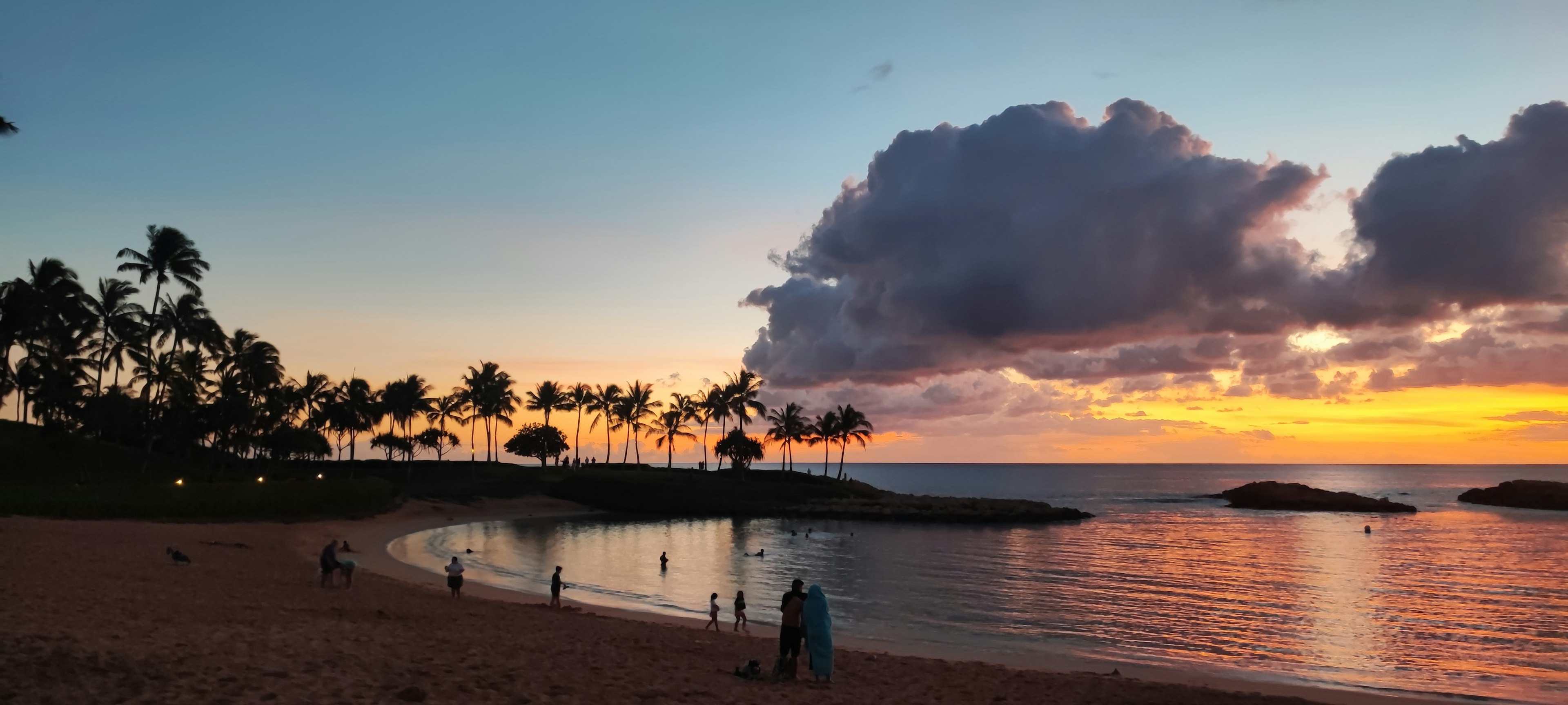 Escena de playa al atardecer con personas disfrutando del agua