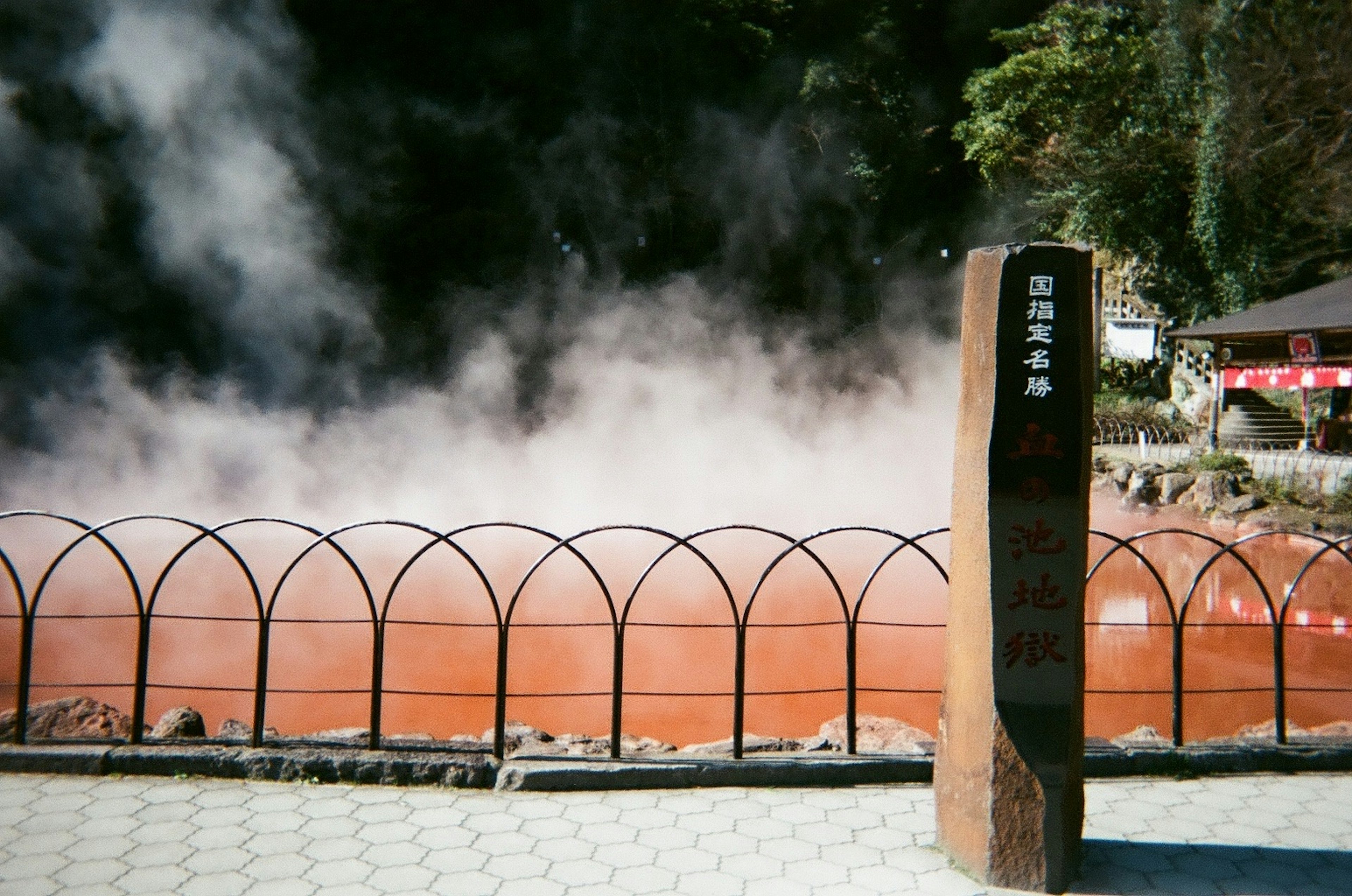 温泉の蒸気が立ち上る紅い池と看板