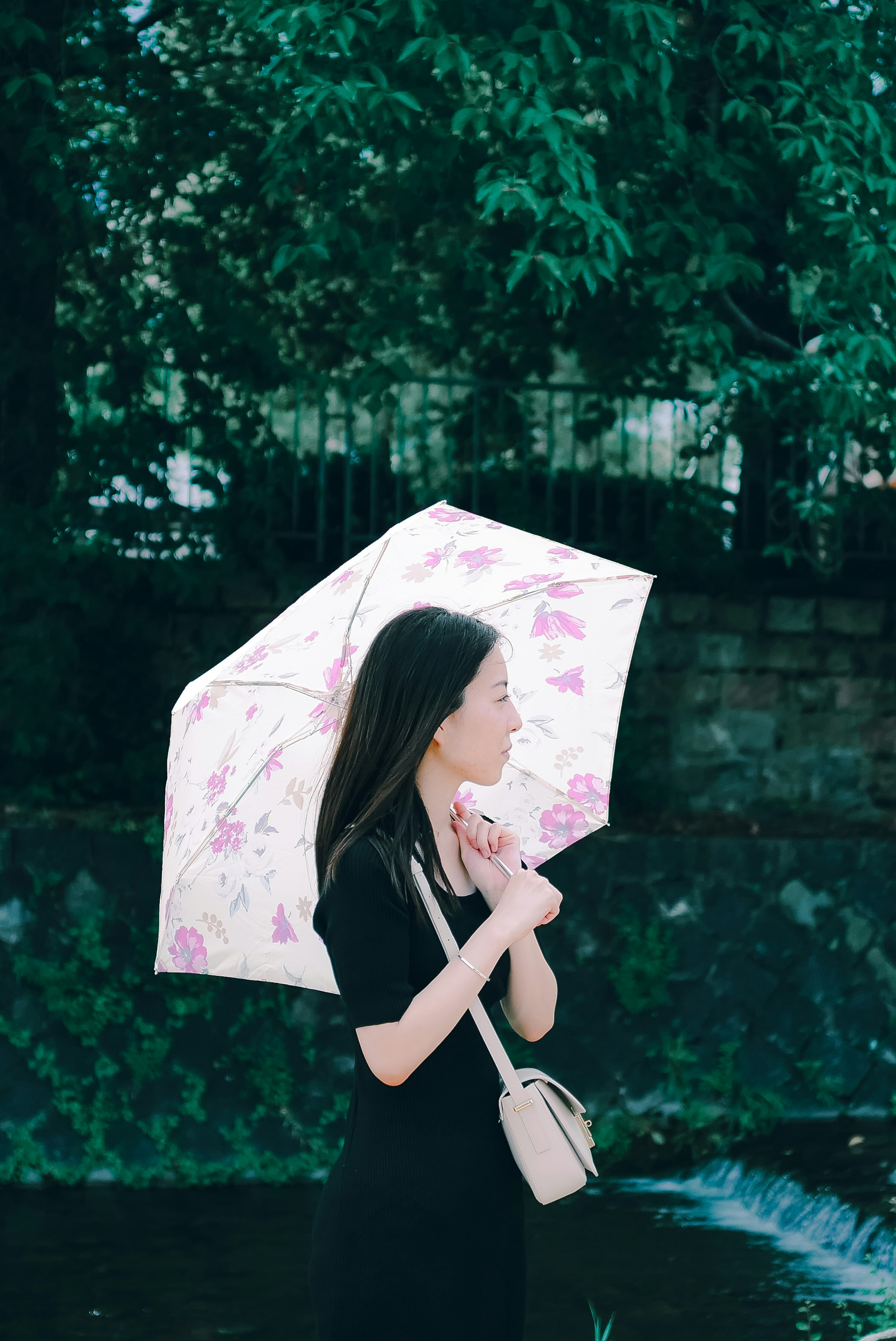 A woman holding a floral umbrella stands in profile