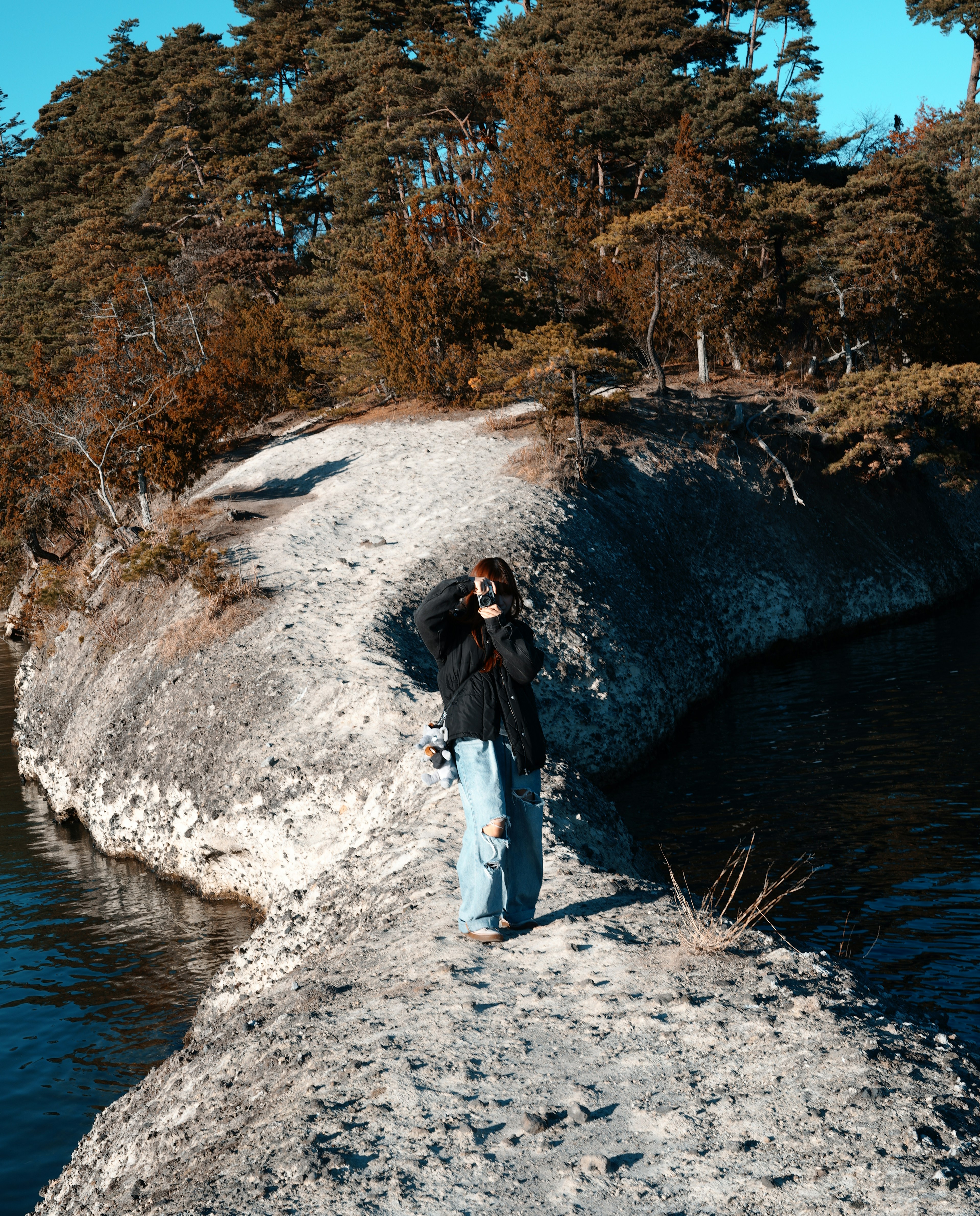 Personne debout sur une rive rocheuse près de l'eau avec des arbres environnants