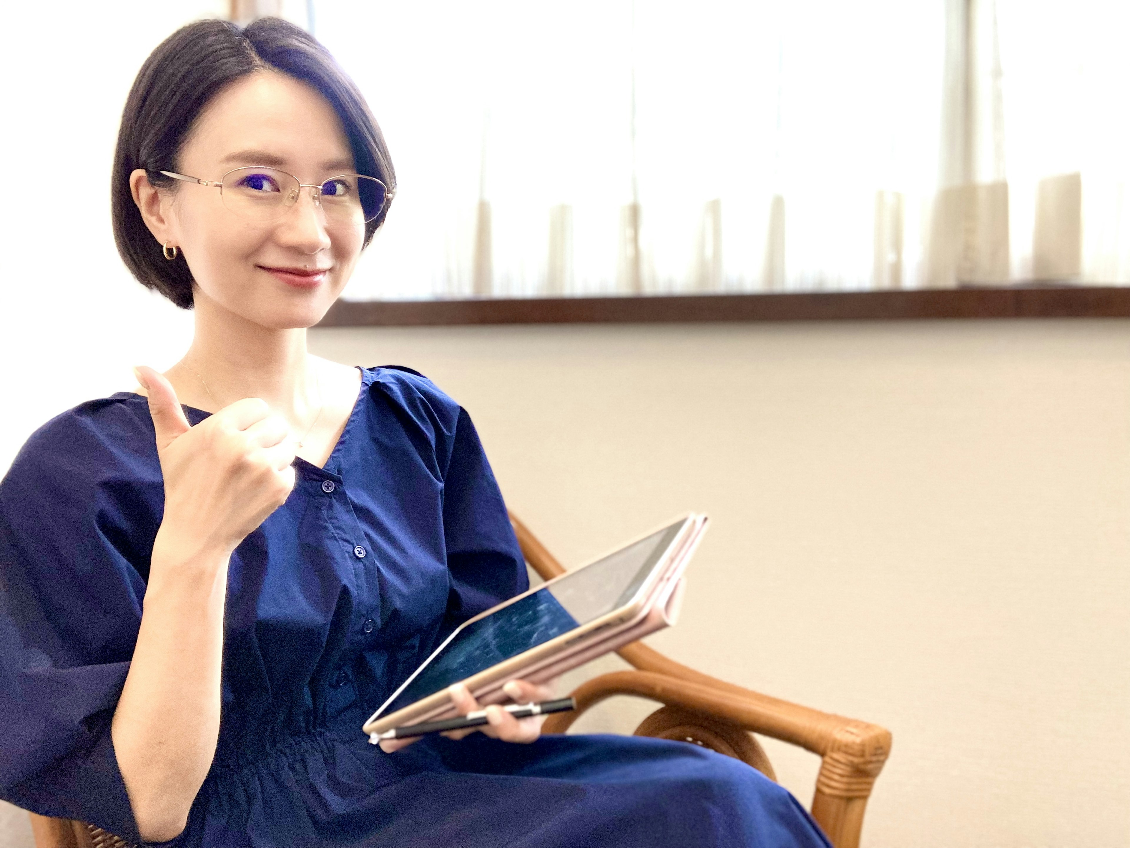 A woman holding a tablet smiling and giving a thumbs up indoors