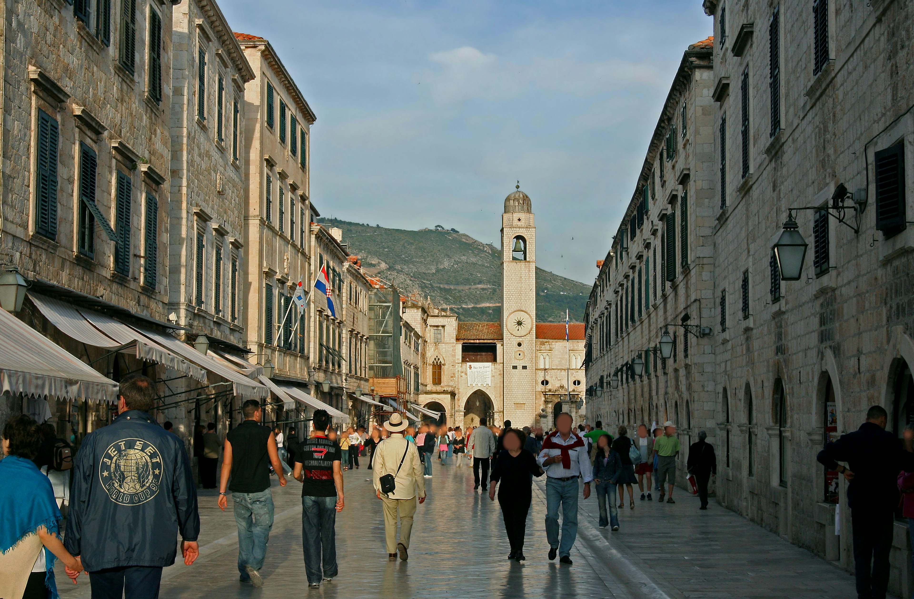 Tourists walking down a street lined with stone buildings featuring a clock tower in the background