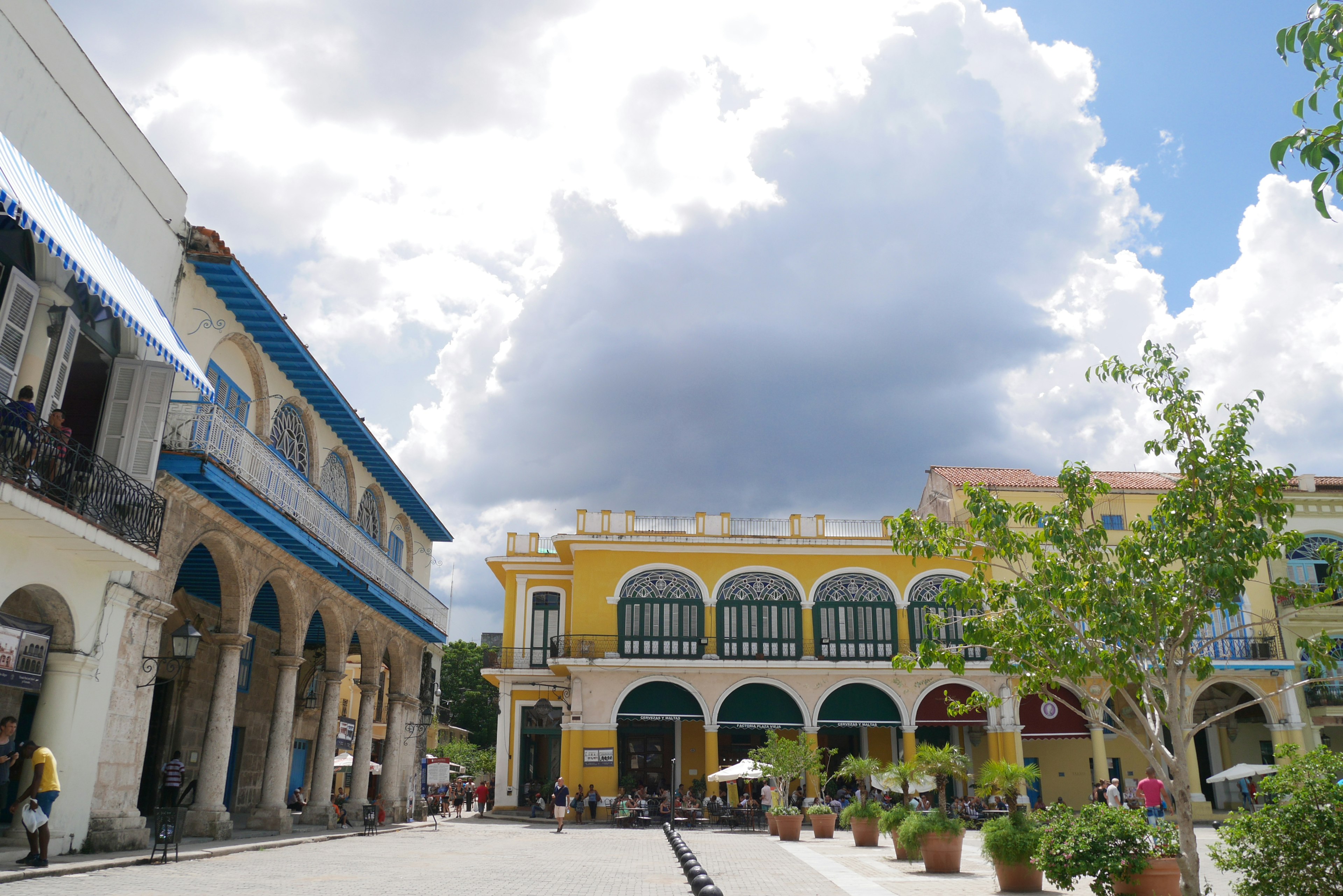 Una piazza vivace con edifici colorati e nuvole drammatiche