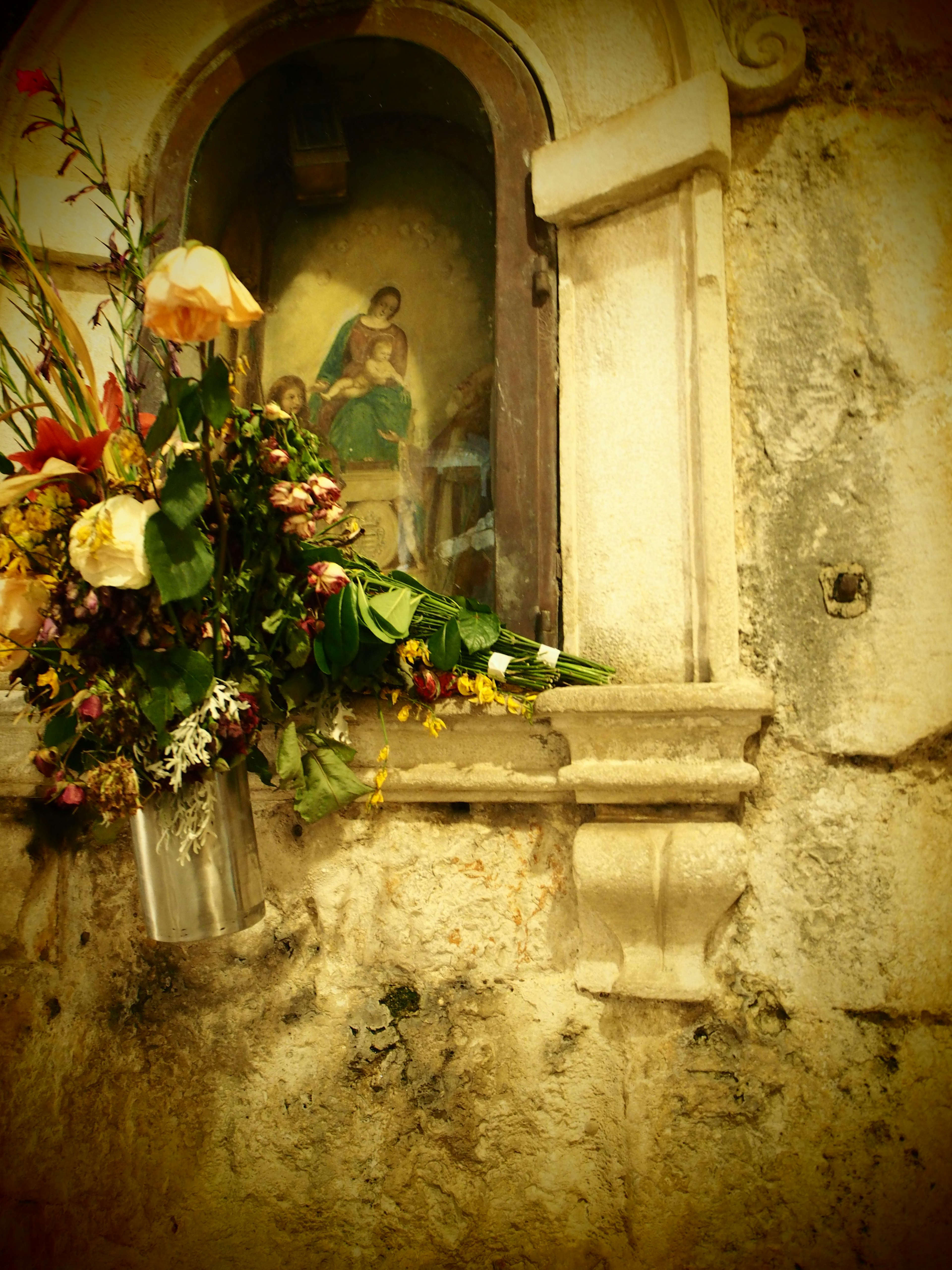 Dekorative Blumen um ein religiöses Gemälde in einer Wandnische