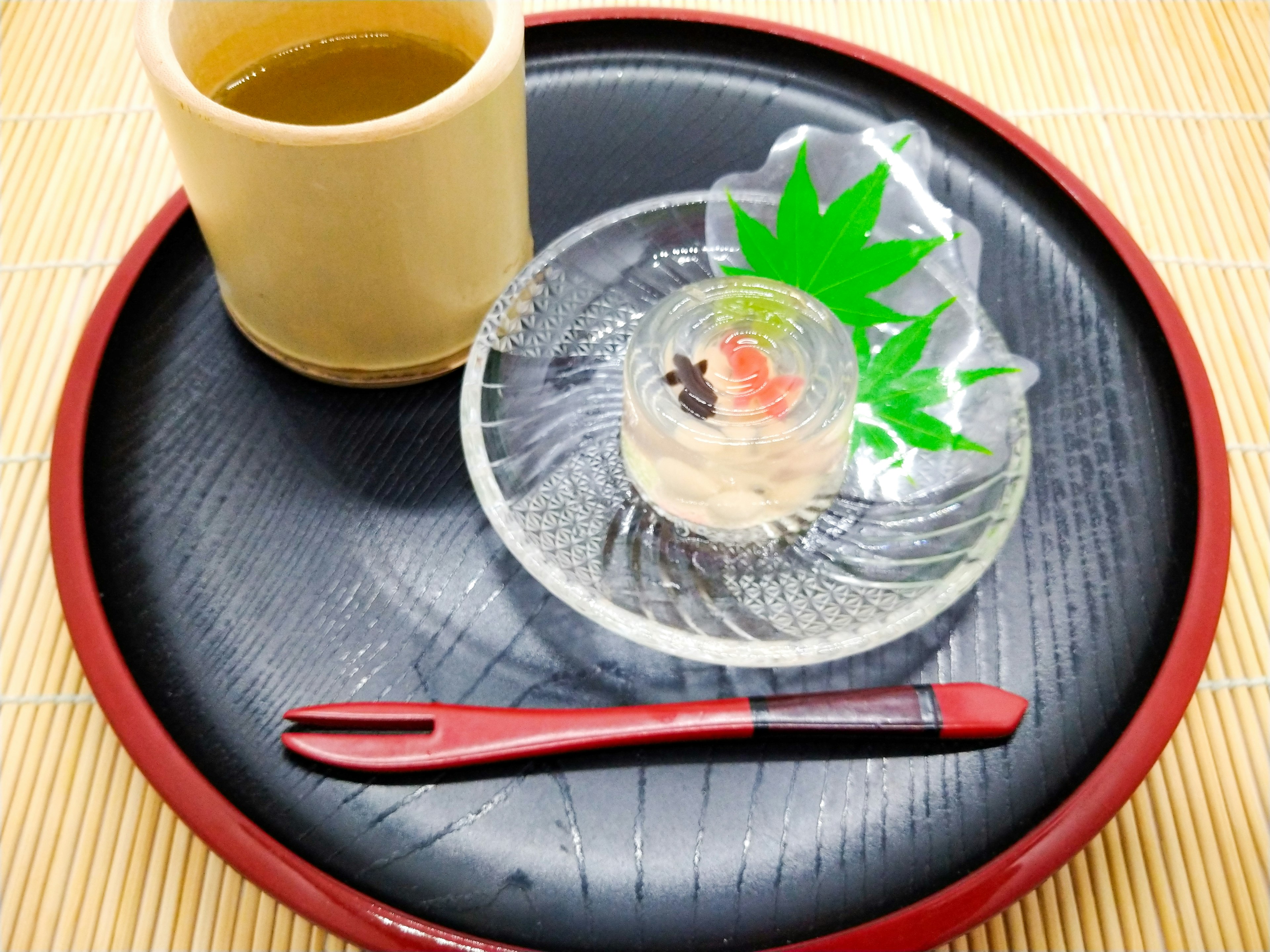 Traditional Japanese tea served with a sweet dessert on a glass plate featuring green leaf decoration and a red chopstick