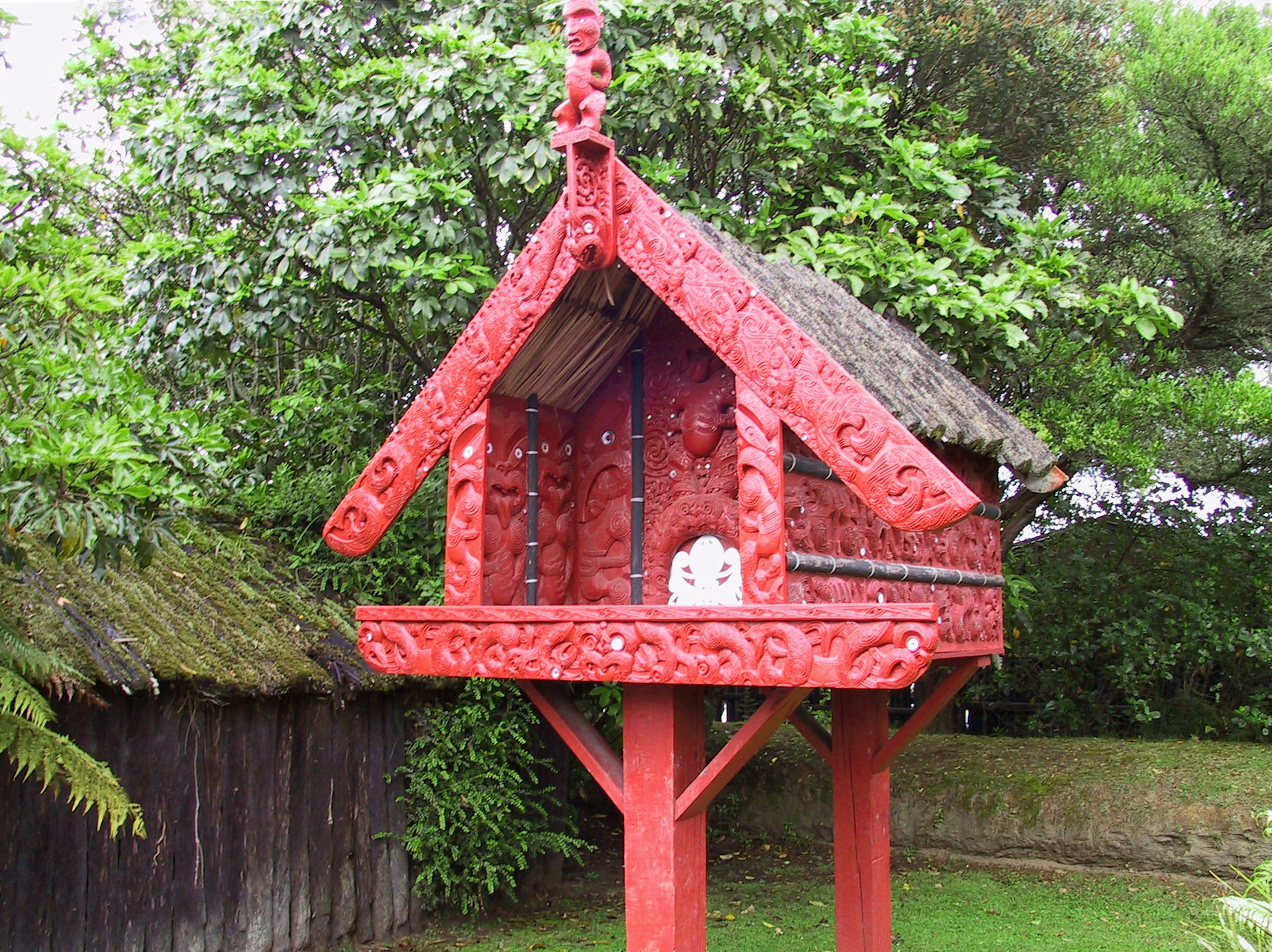 Traditional red carved house model surrounded by green trees