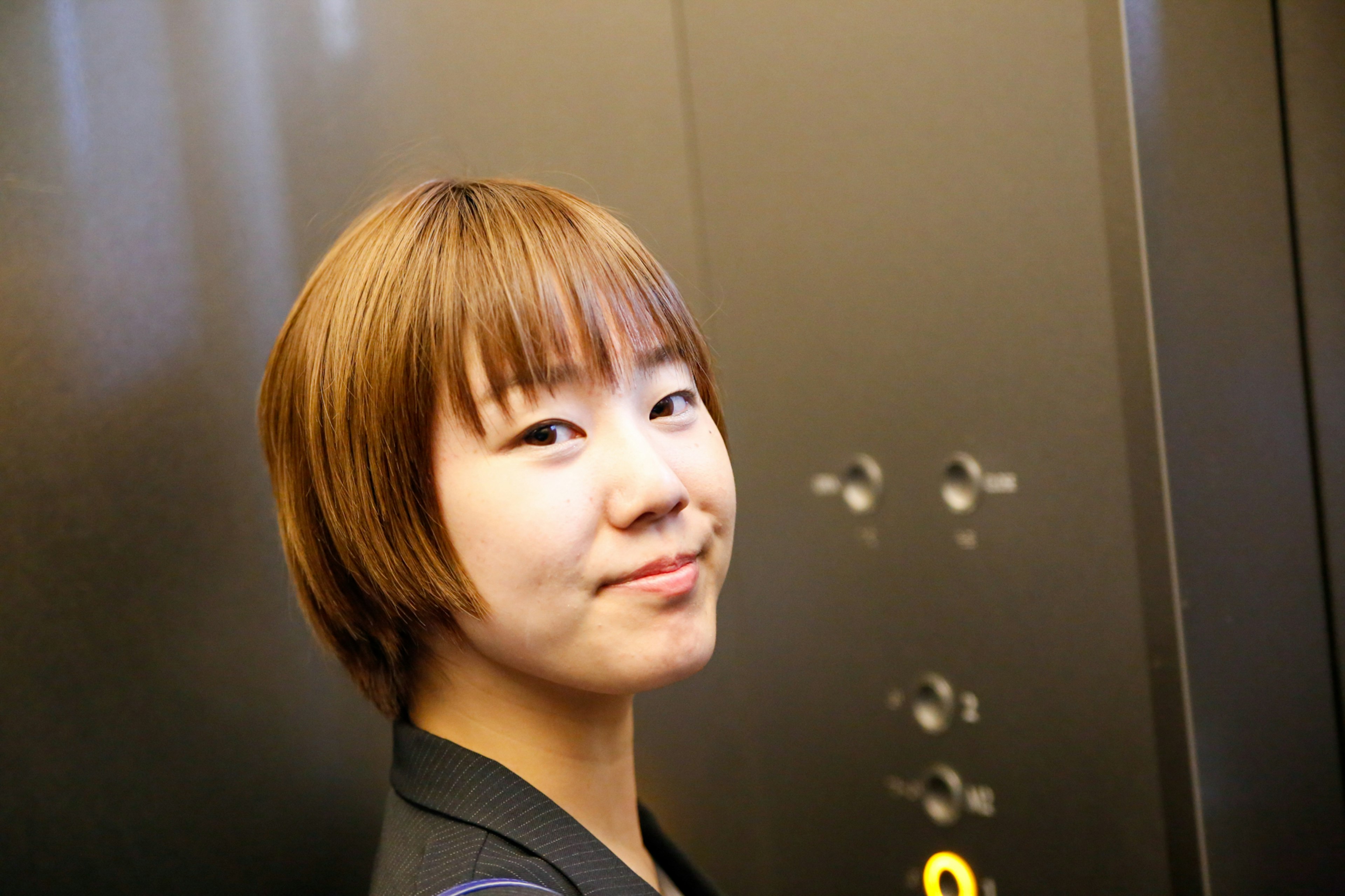 Close-up of a woman in an elevator with short brown hair and a cheerful smile