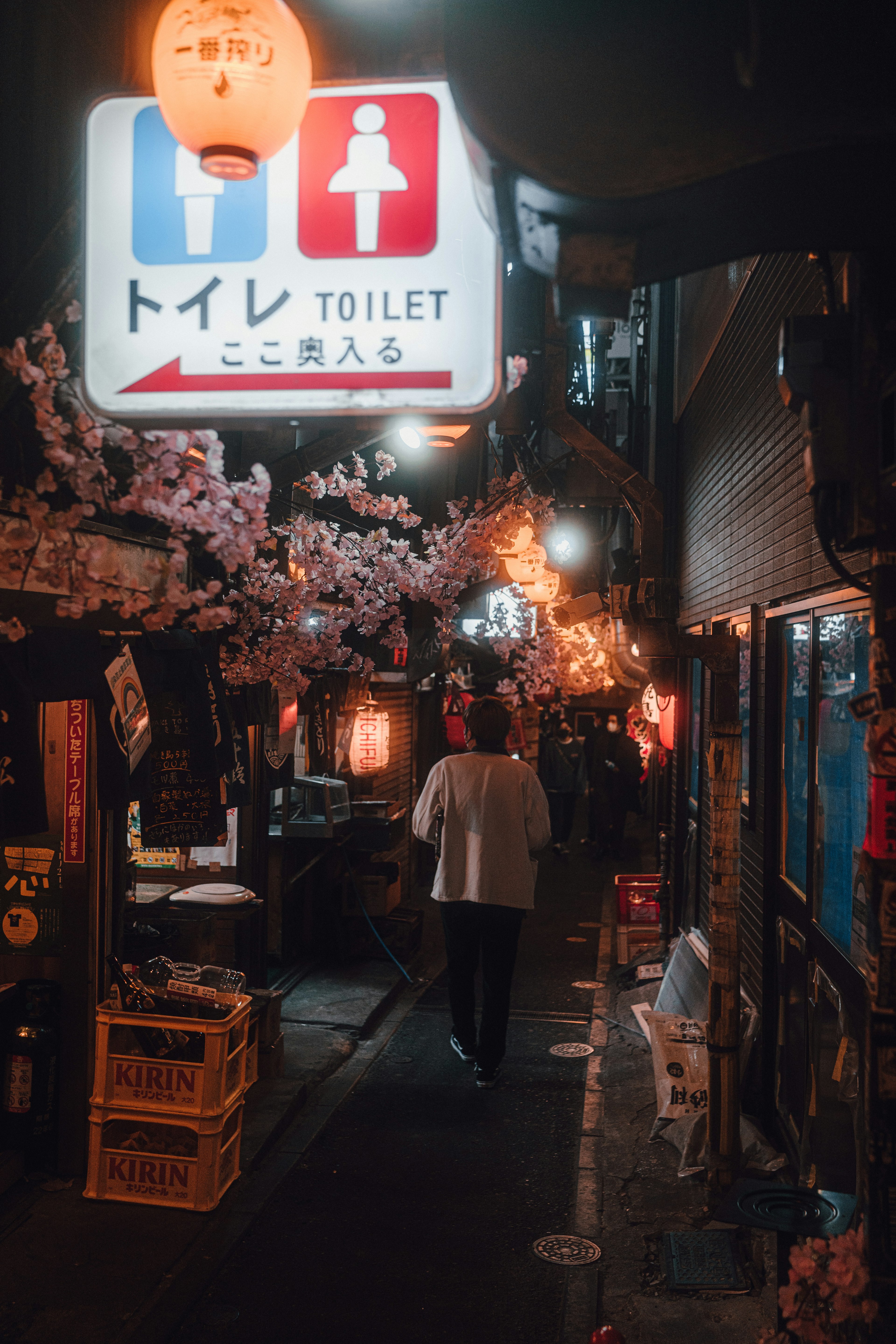 夜の街並みを歩く人と桜の装飾があるトイレの看板