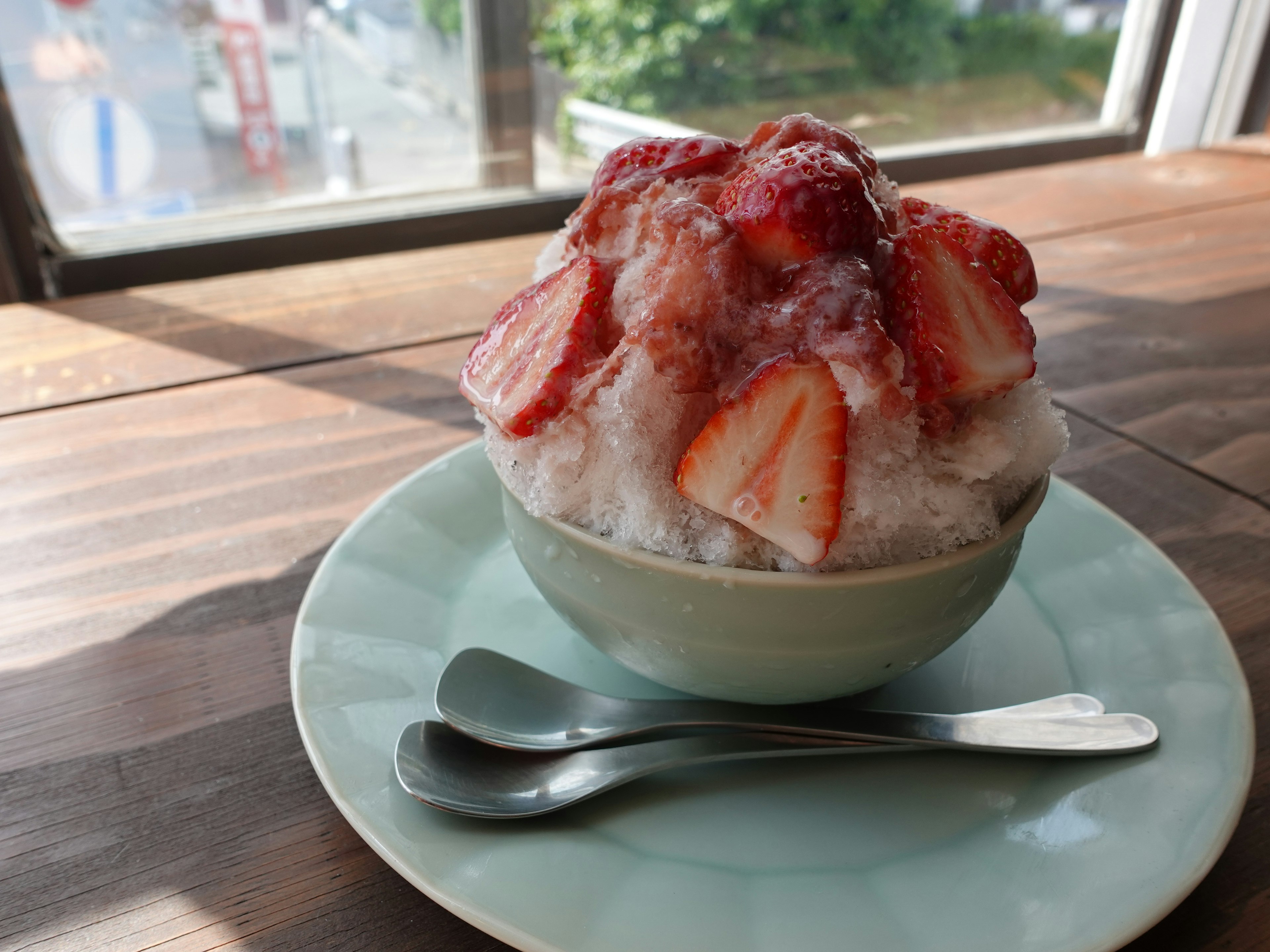 Bol de glace pilée surmonté de fraises sur une table en bois