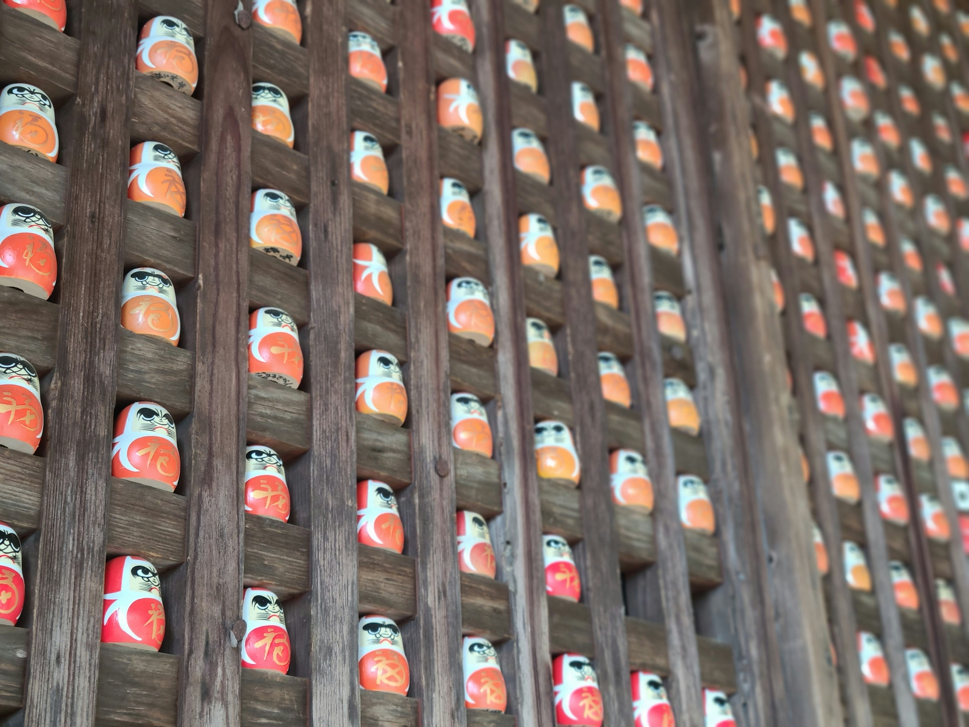 Muñecas Daruma coloridas dispuestas en una pared de madera