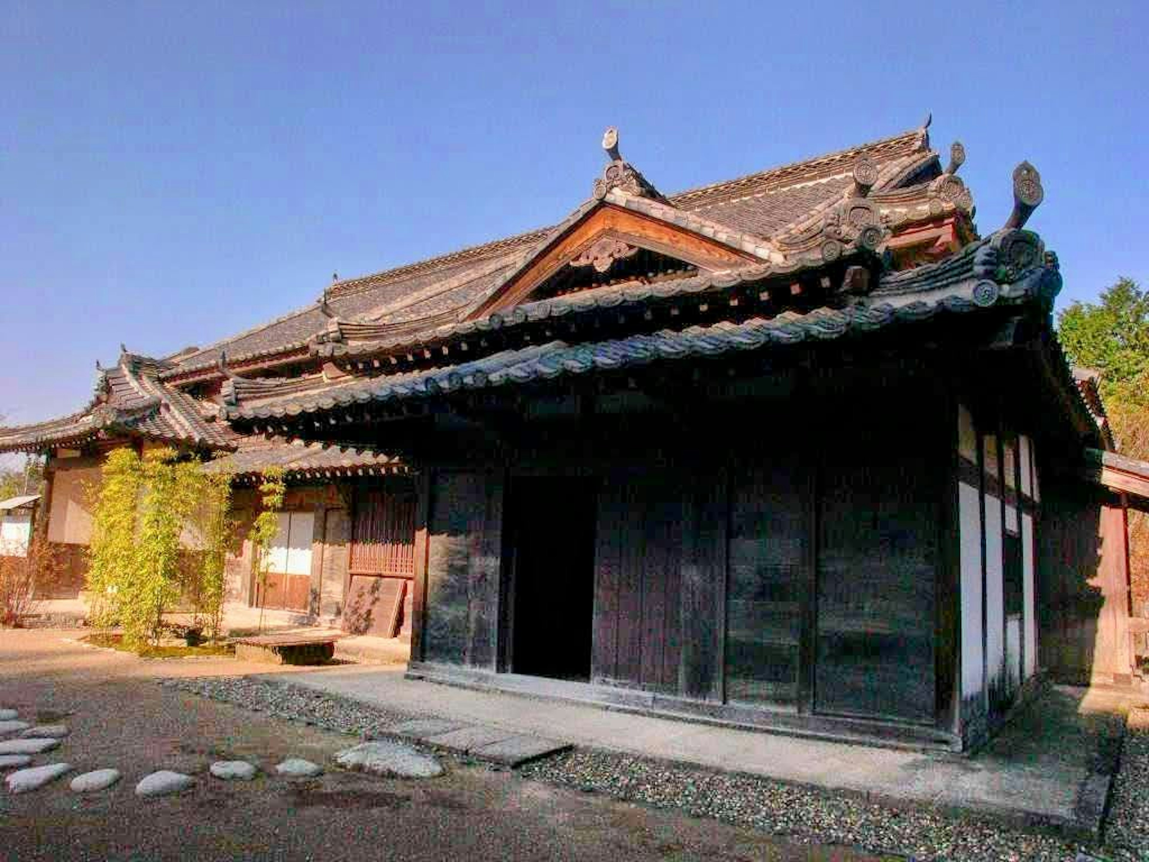 Extérieur d'une maison japonaise traditionnelle avec une architecture en bois et un toit en tuiles entouré de verdure