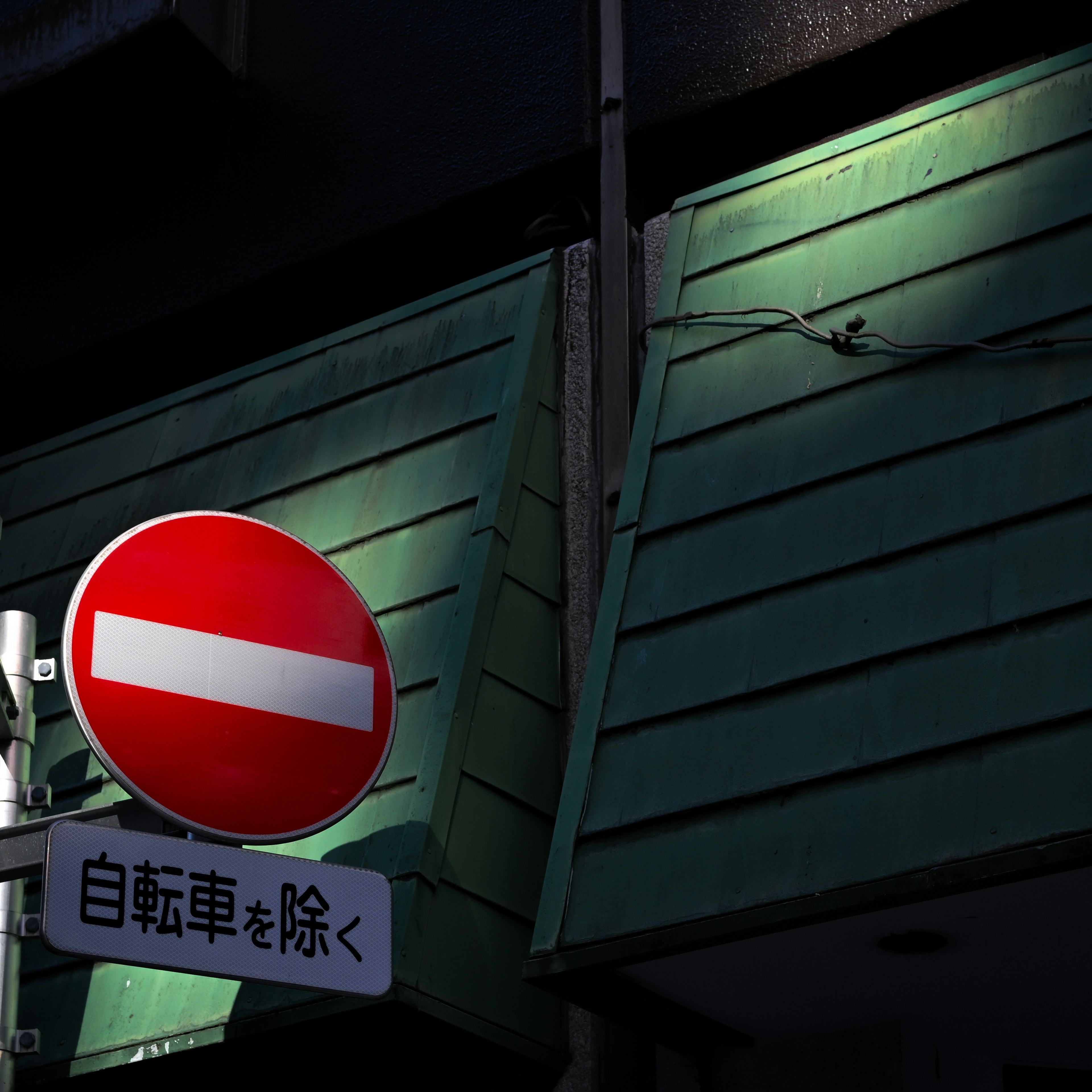 Red no entry sign against a green wooden wall in urban setting