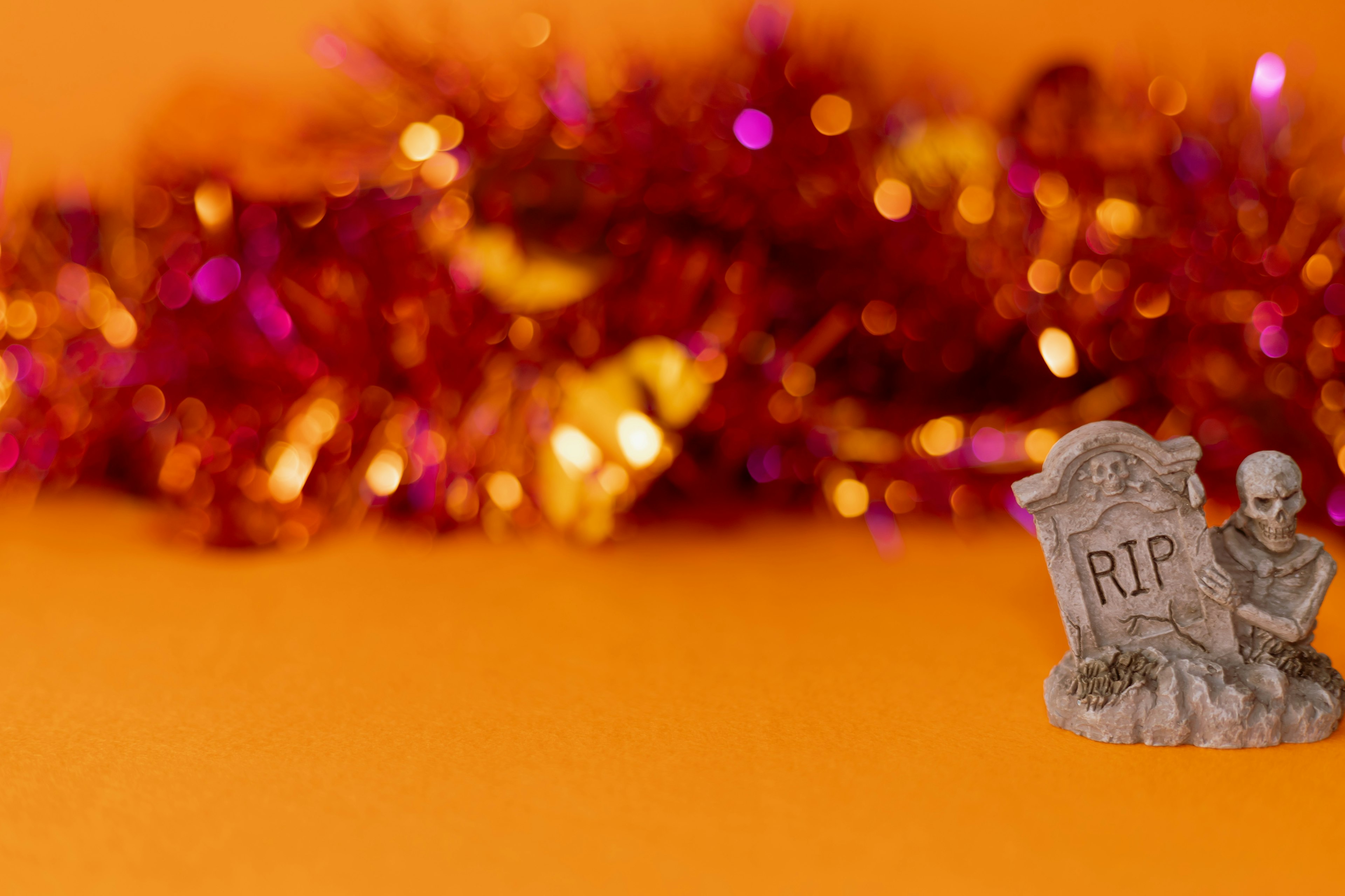 An orange background with purple and gold tinsel featuring a gravestone and skeleton decoration