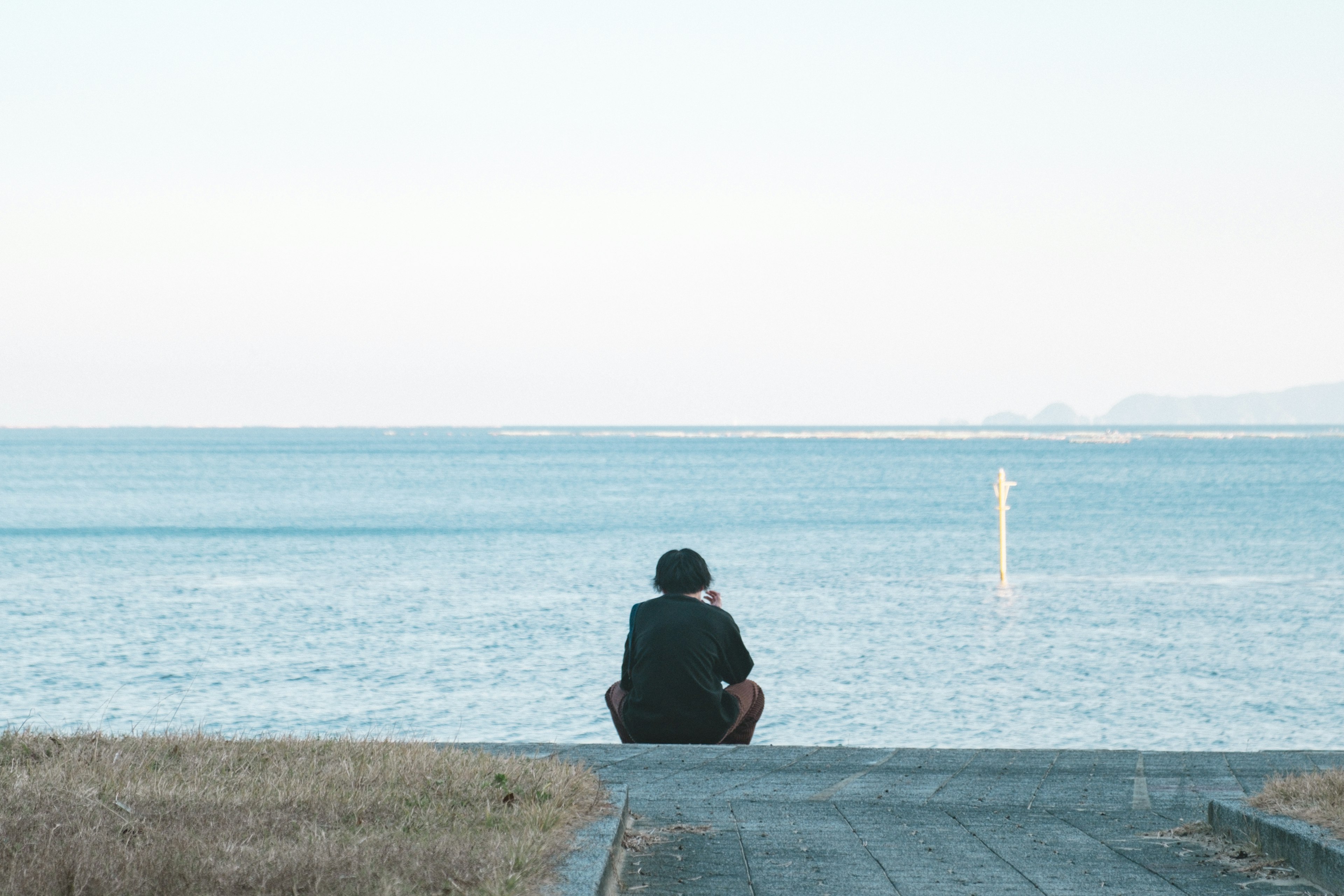 Ein Junge sitzt auf einem Weg und schaut auf das Meer