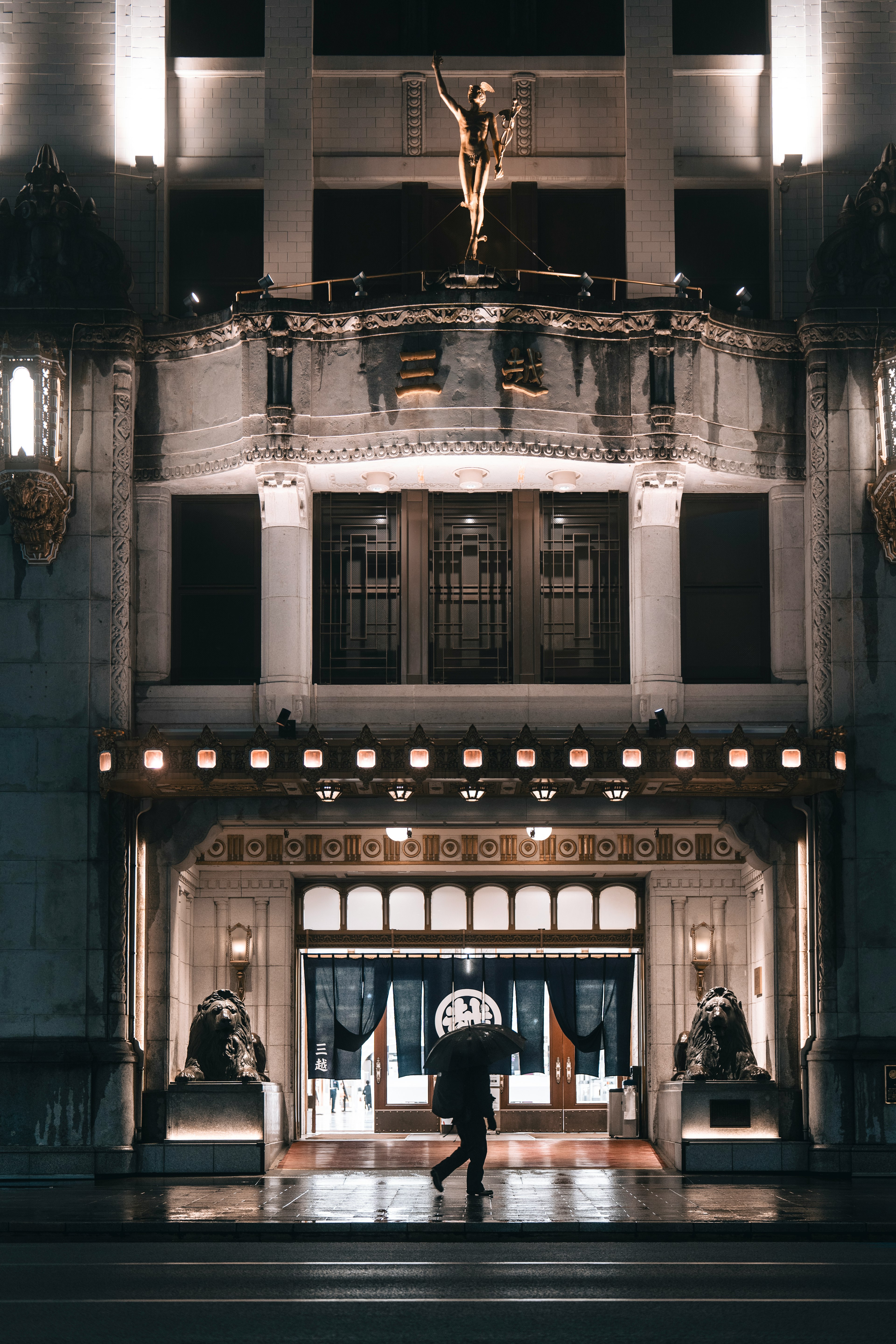 A person with an umbrella walking towards a luxurious hotel entrance at night