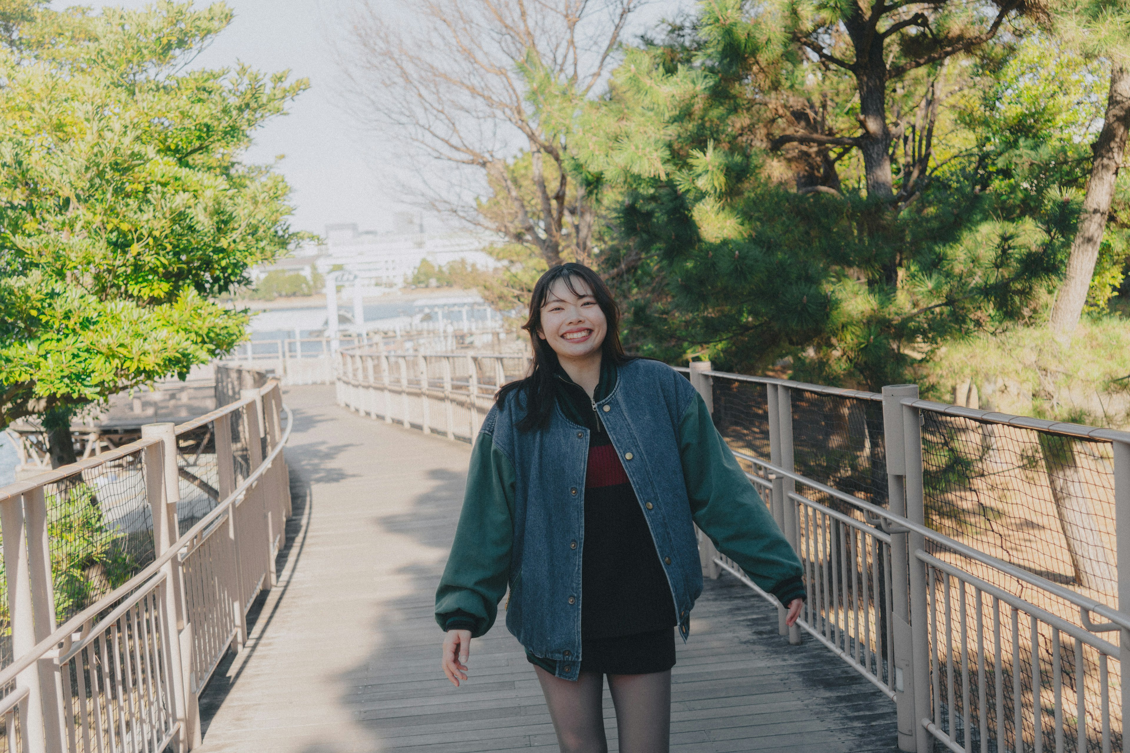 緑の木々に囲まれた歩道を歩く笑顔の女性