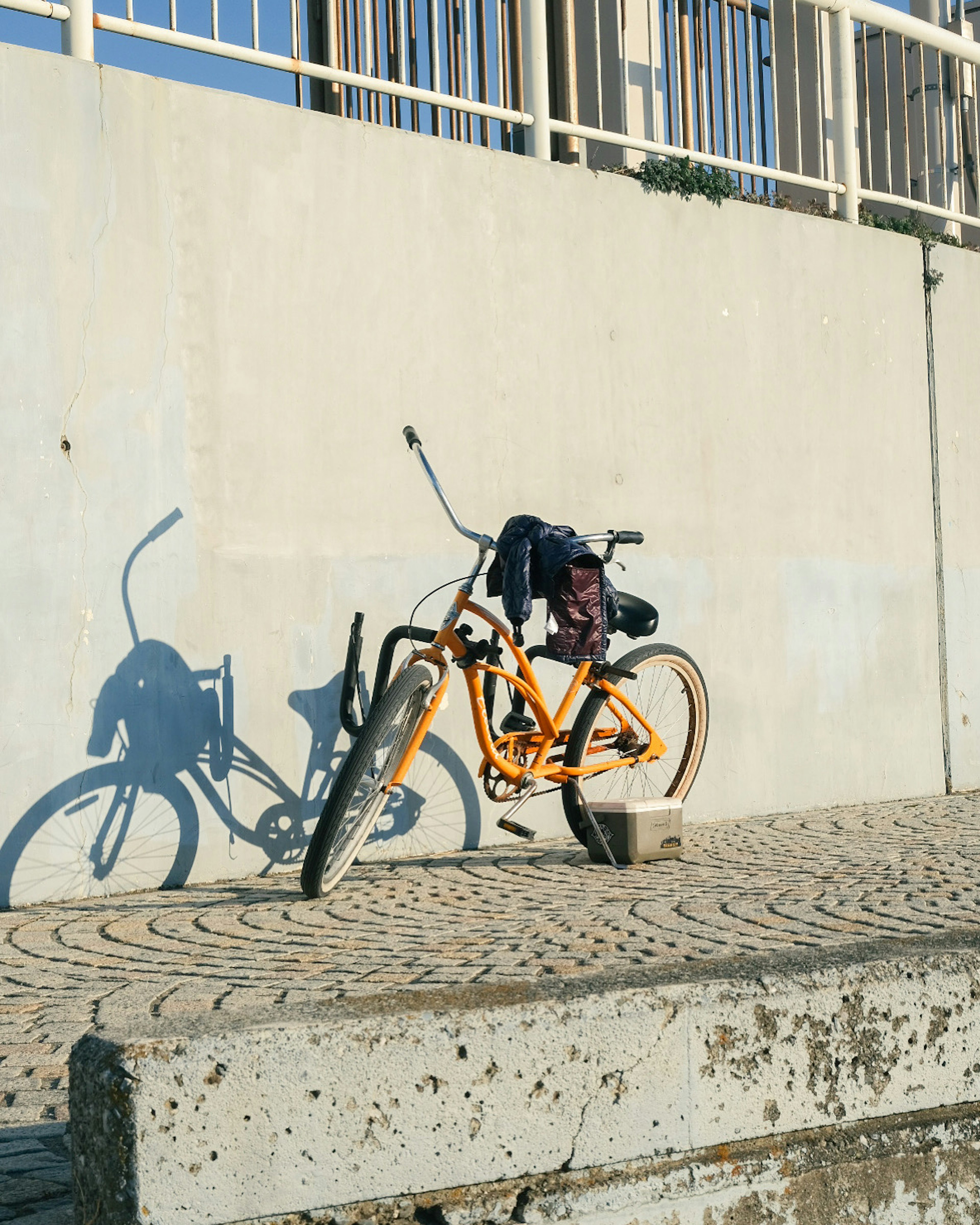 Ein orangefarbenes Fahrrad lehnt an einer Wand und wirft einen Schatten