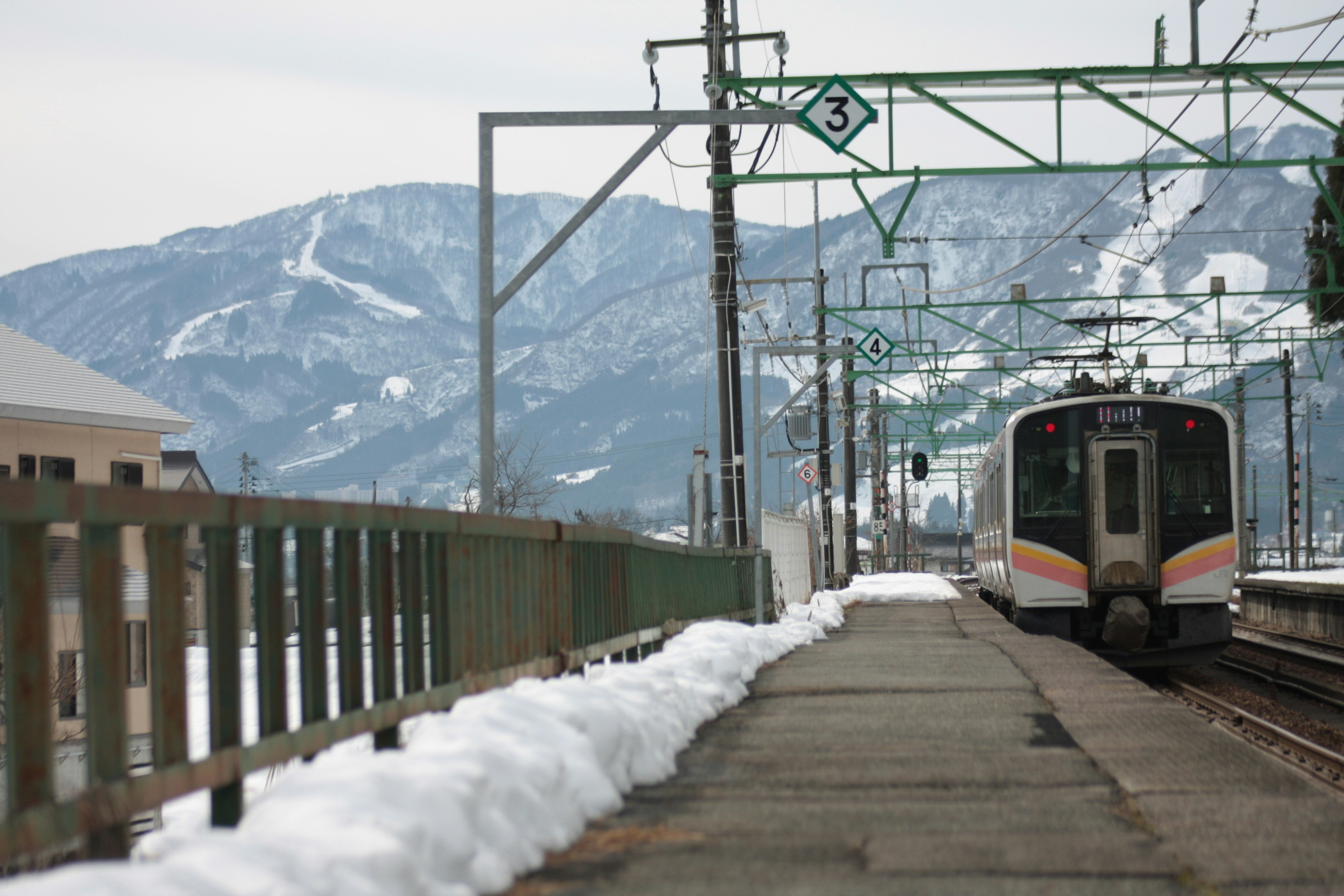 Train arrivant à une gare enneigée avec des montagnes en arrière-plan